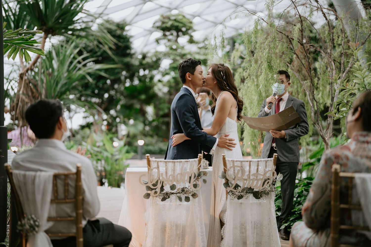Elegant outdoor wedding reception setup with tropical greenery and white table settings.