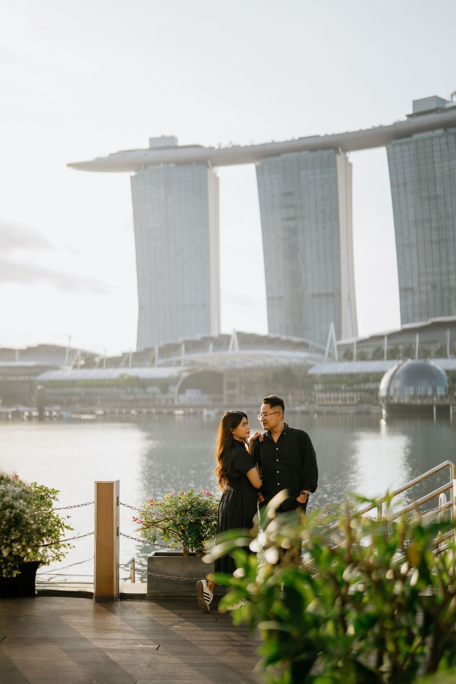 Couple posing romantically on waterfront promenade with Marina Bay Sands hotel backdrop in Singapore.