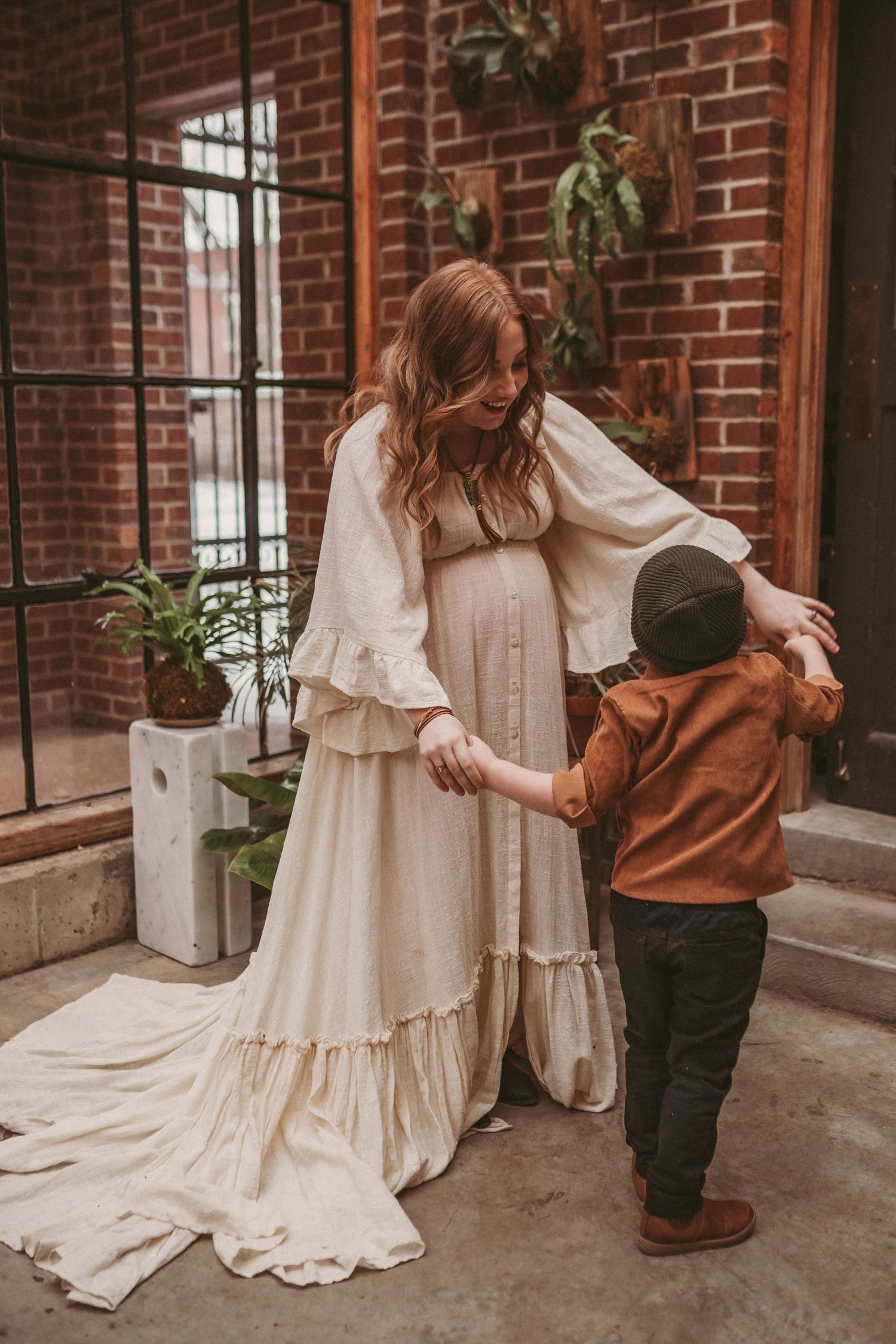A pregnant mother dances with her son inside a brick building, photographed by Kristy Baker Photography.