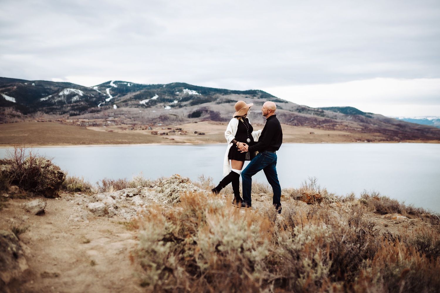 A couple on top of a hill standing and cradling the woman's pregnant belly, photographed by Kristy Baker Photography in Steamboat Springs.