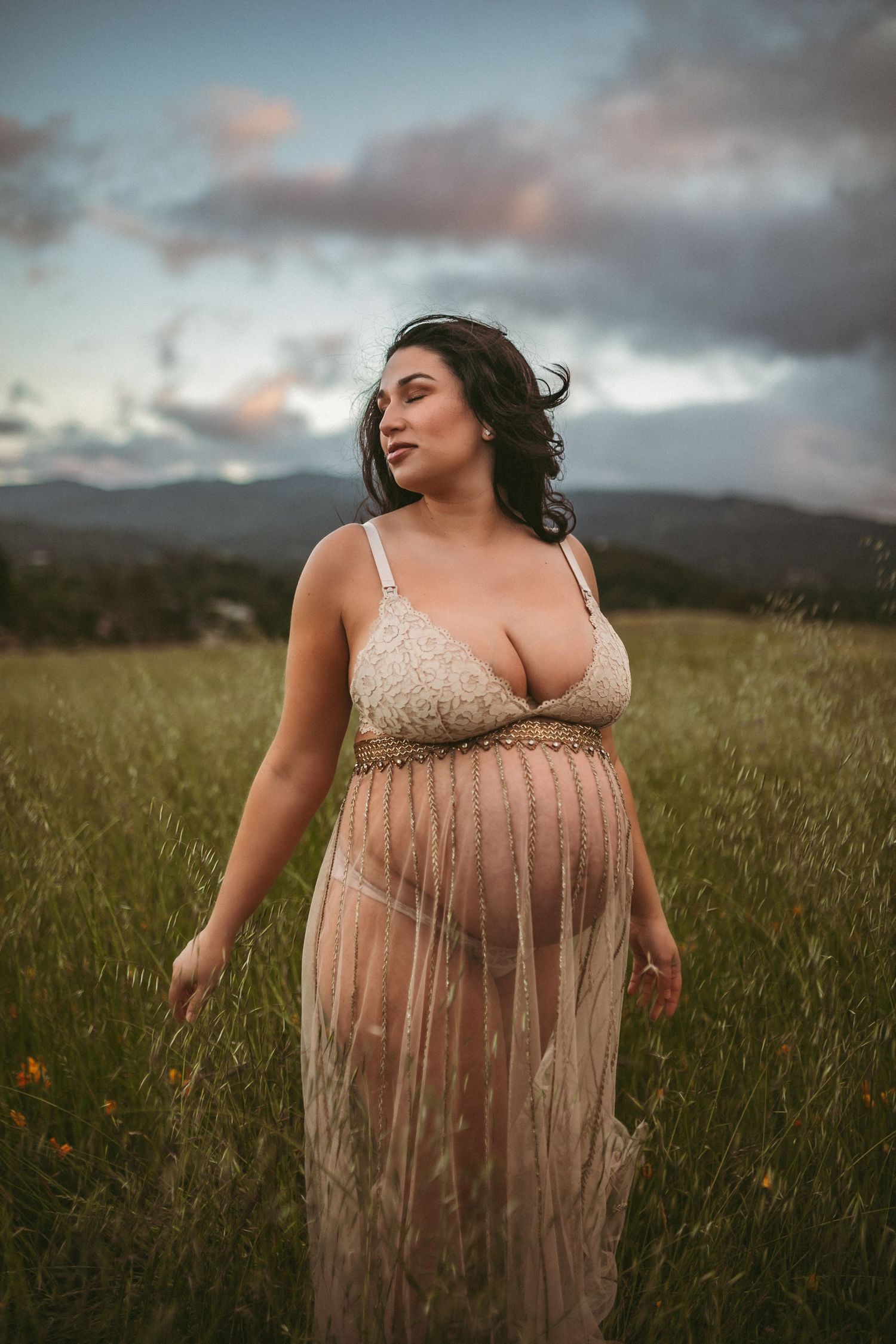 A woman's hair blows in the wind as she looks down at her pregnant belly, photographed by Kristy Baker Photography.