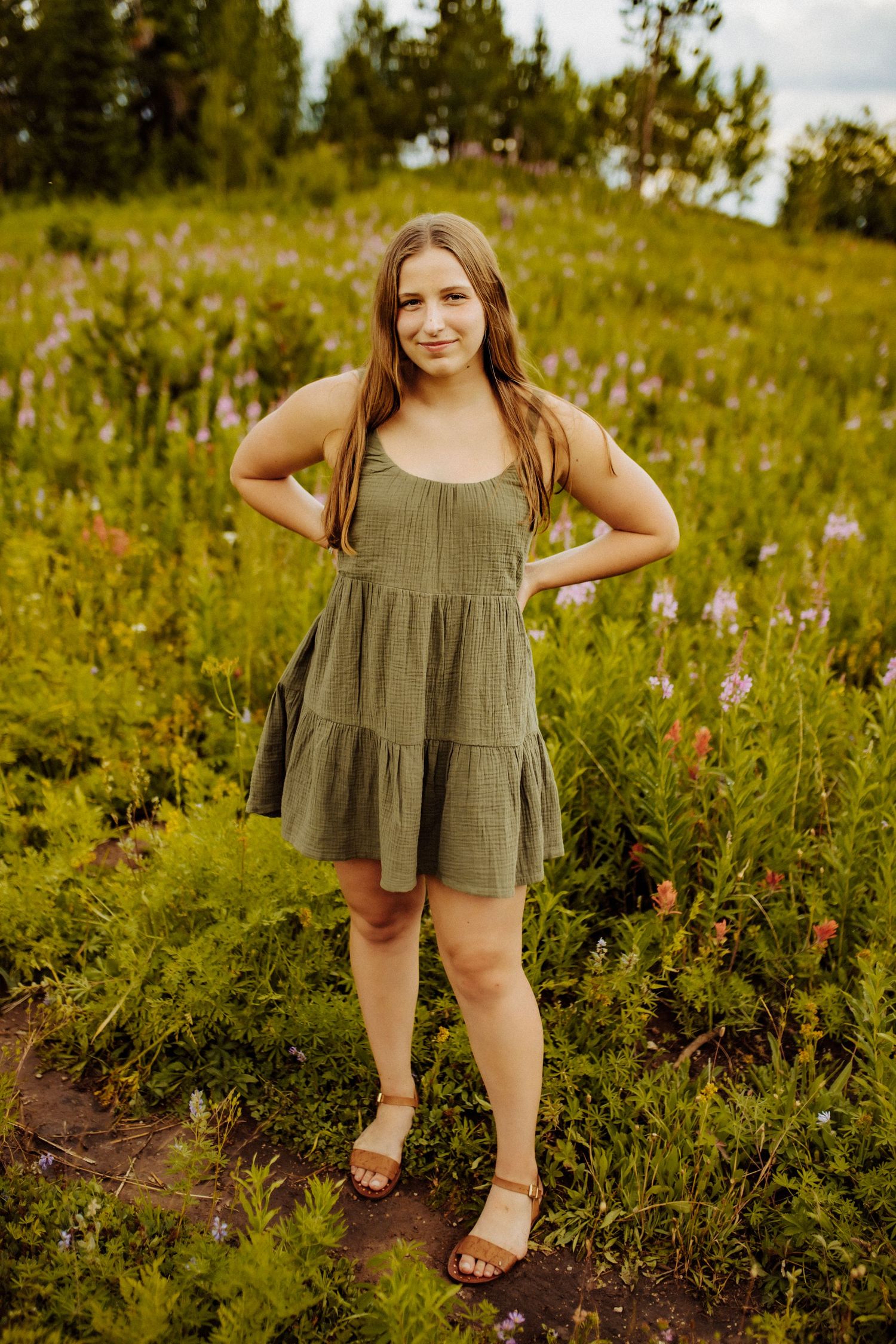 A high school senior girl poses in the grass wearing an olive green dress.