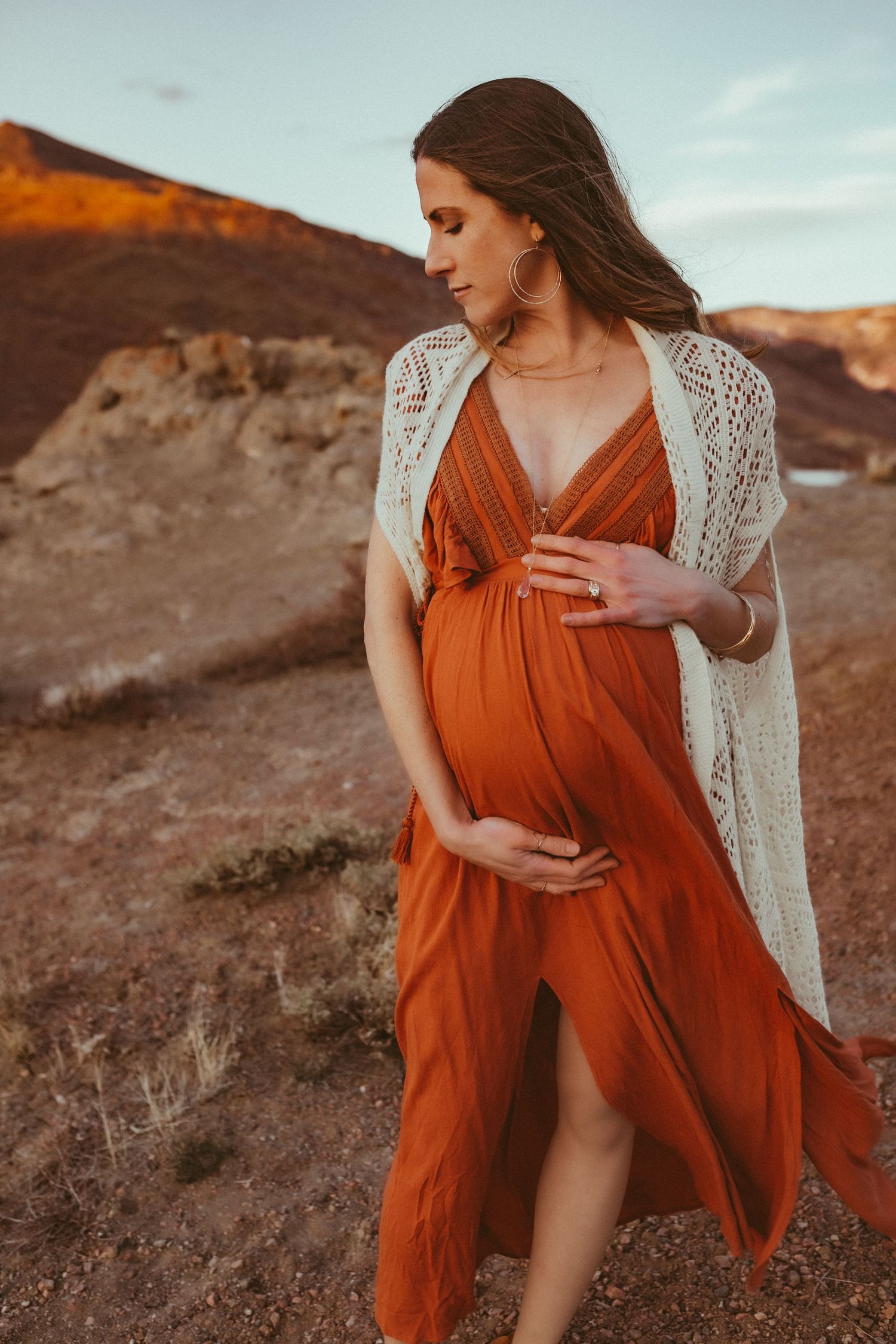 A pregnant woman in a red dress cradling her belly, photographed by Kristy Baker Photography in Steamboat Springs, Colorado.