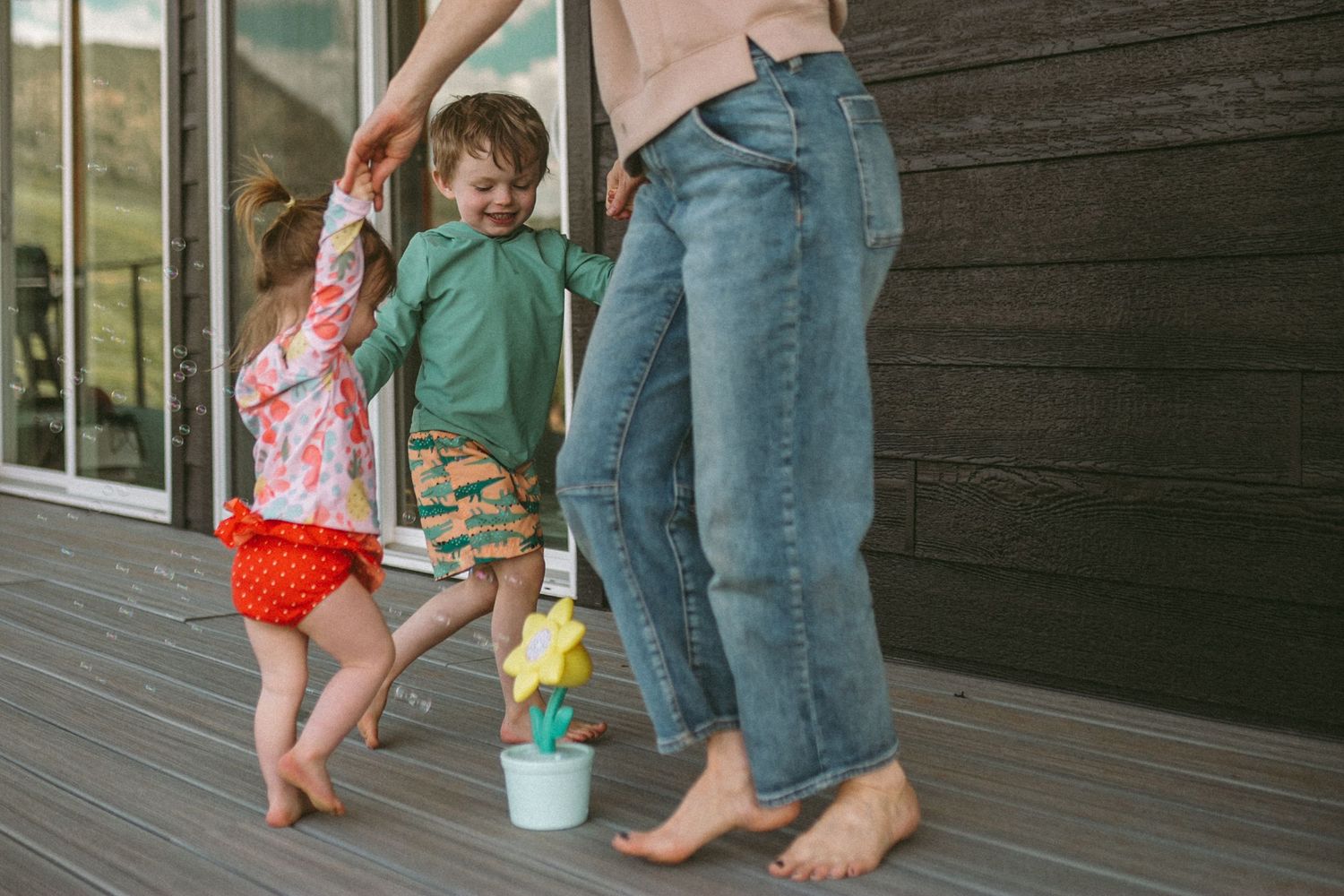 A mother and her two children hold hands and dance around a flower bubble machine, photographed by Kristy Baker Photography.