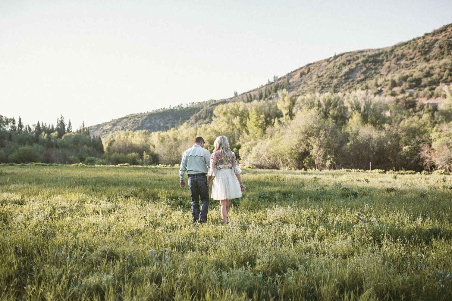 A couple walking away in a big green field, photographed by Kristy Baker Photography in Steamboat Springs, Colorado.