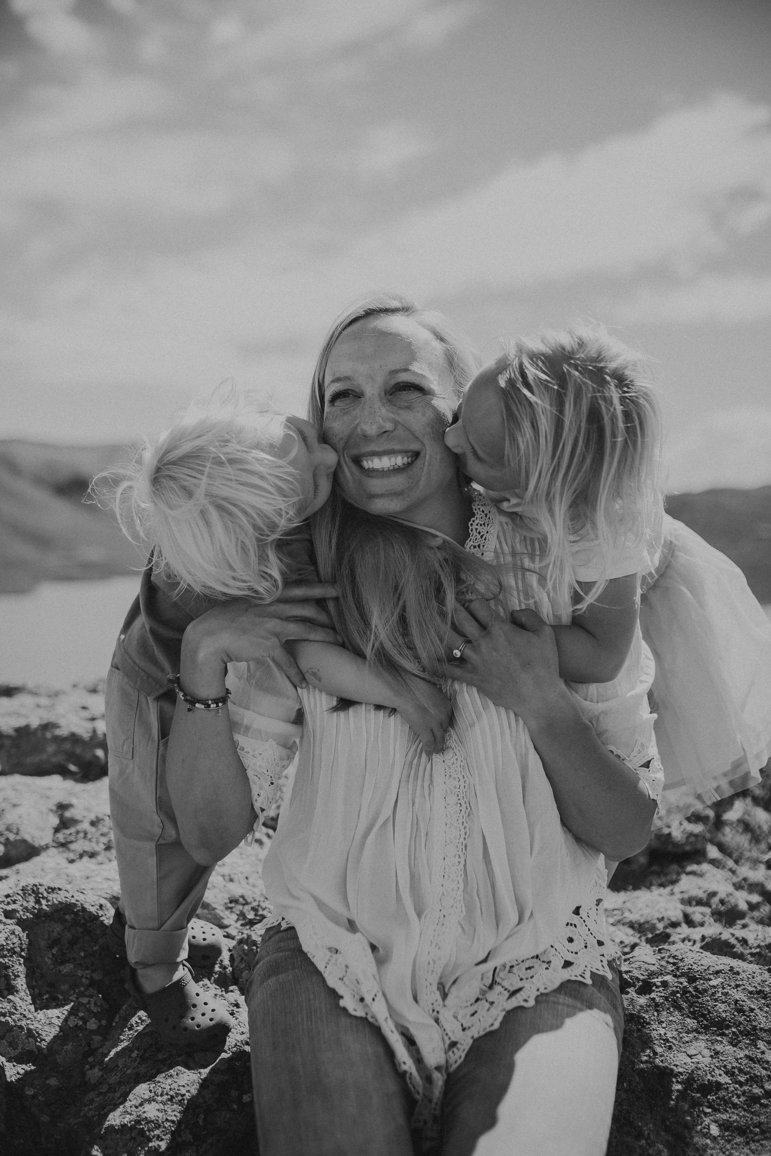 A mother is smiling while she is kissed on the cheeks by her son and daughter, photographed by Kristy Baker Photography.