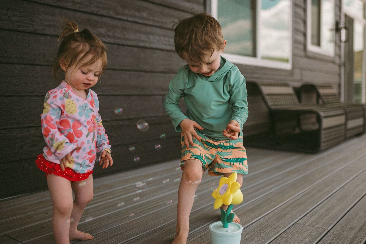 A young boy and girl are in swimwear playing with a bubble machine, photographed by Kristy Baker Photography.