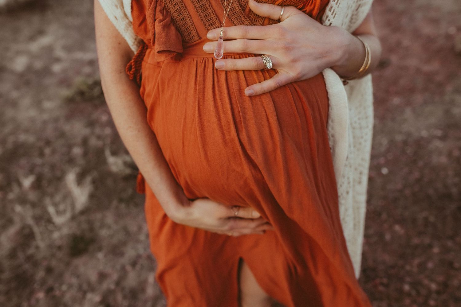 A pregnant woman in a red dress cradling her belly, photographed by Kristy Baker Photography in Steamboat Springs, Colorado.