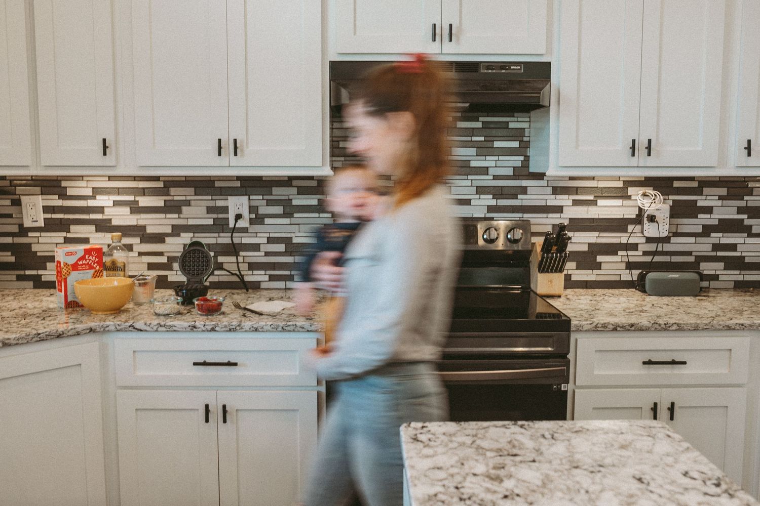 A mother carrying her little girl is walking across the kitchen, photographed by Kristy Baker Photography in Steamboat Springs, CO.