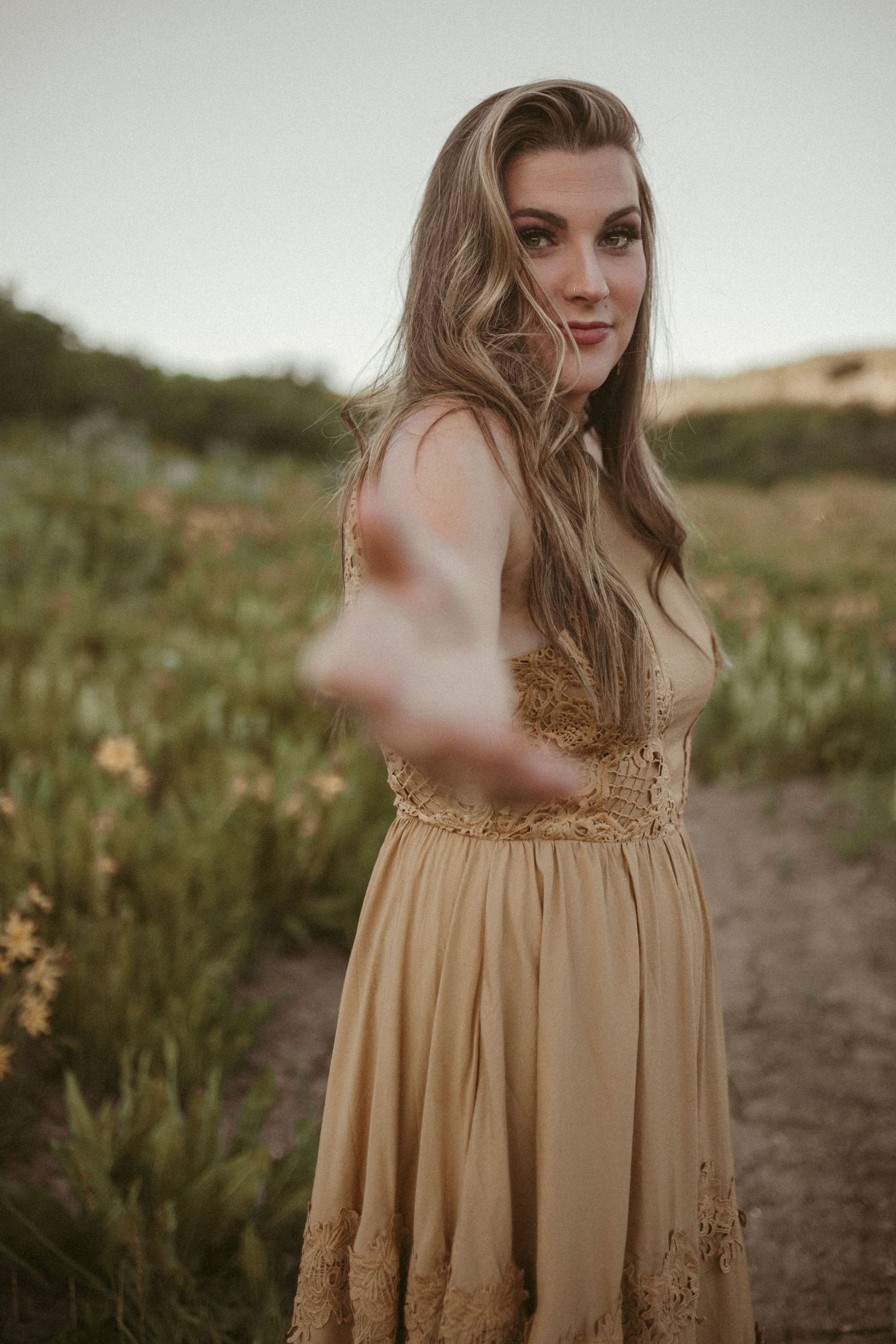 A woman wearing a yellow dress reaches out her hand towards the camera.