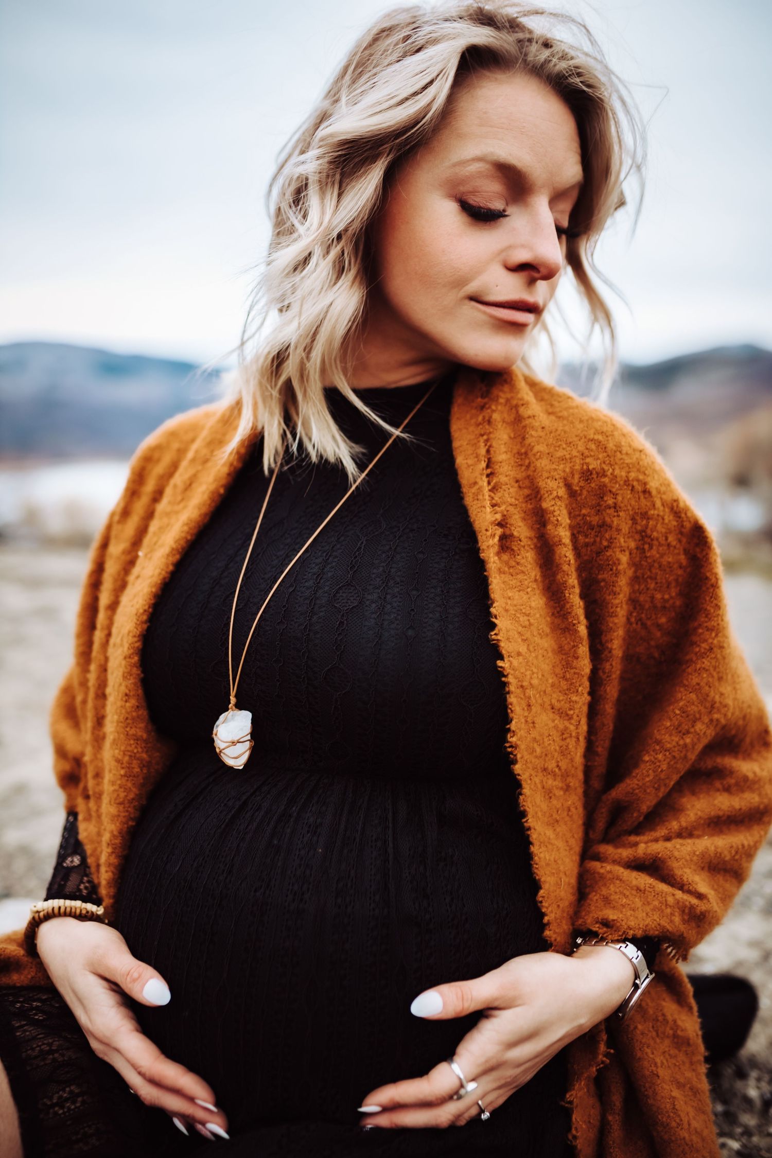 A woman in black closing her eyes and cradling her pregnant belly, photographed by Kristy Baker Photography in Steamboat Springs, Colorado.