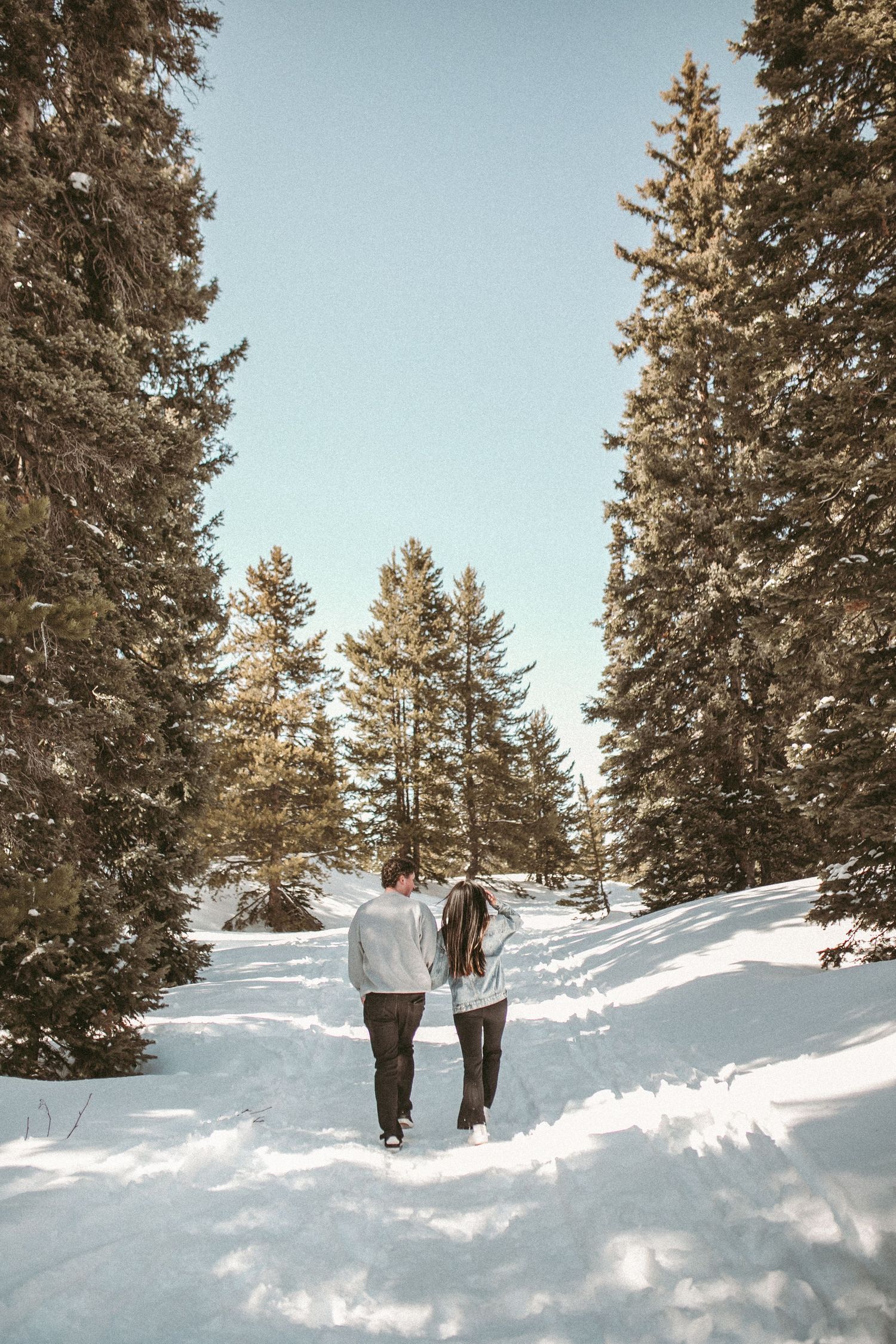 A couple walking together through the forrest in the winter, photographed by Kristy Baker Photography in Steamboat Springs, Colorado.