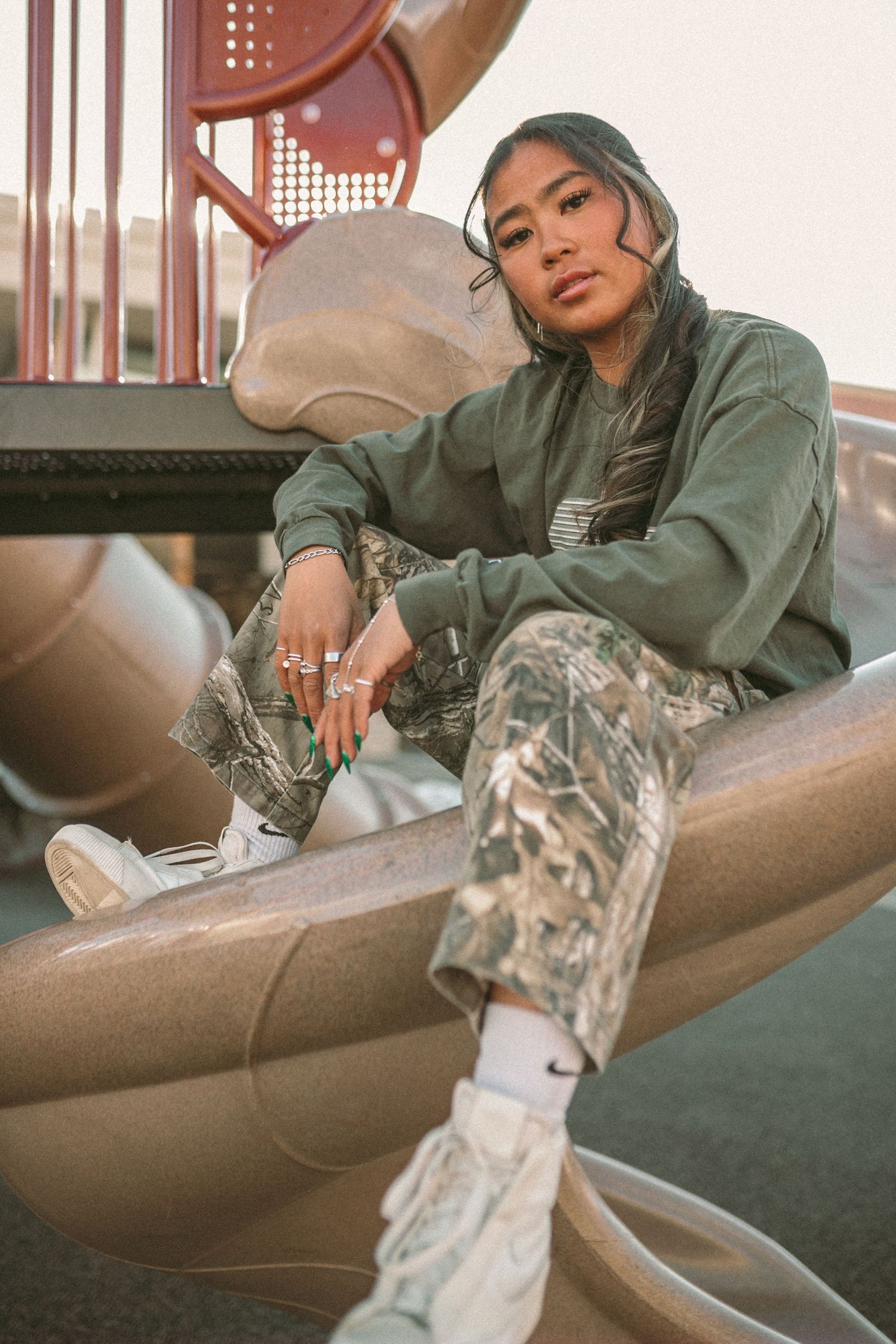 A woman stares into the camera lens as she sits upon a slide at the park.