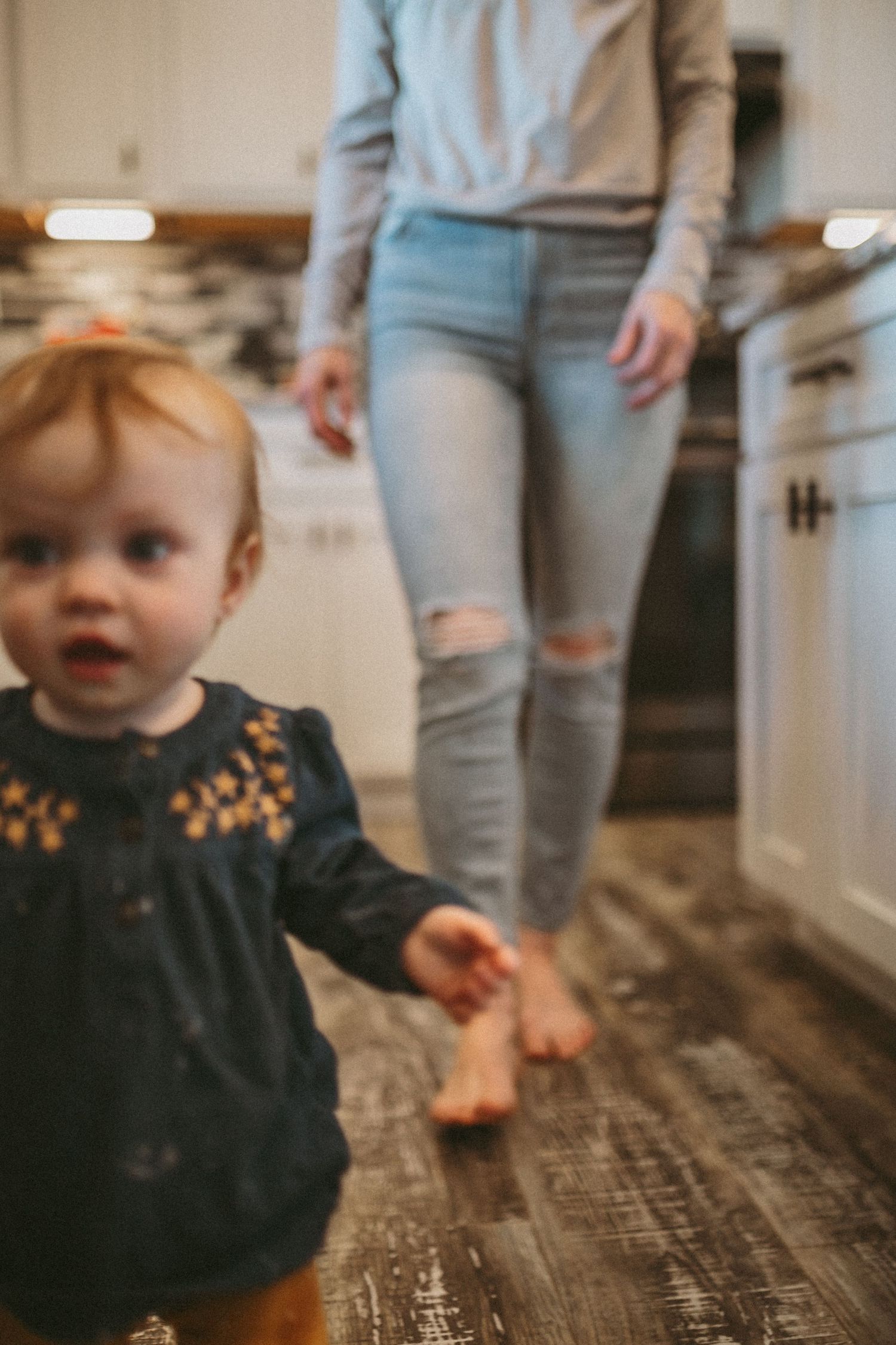A little girl walking towards the camera with her mother following behind her, photographed by Kristy Baker Photography.