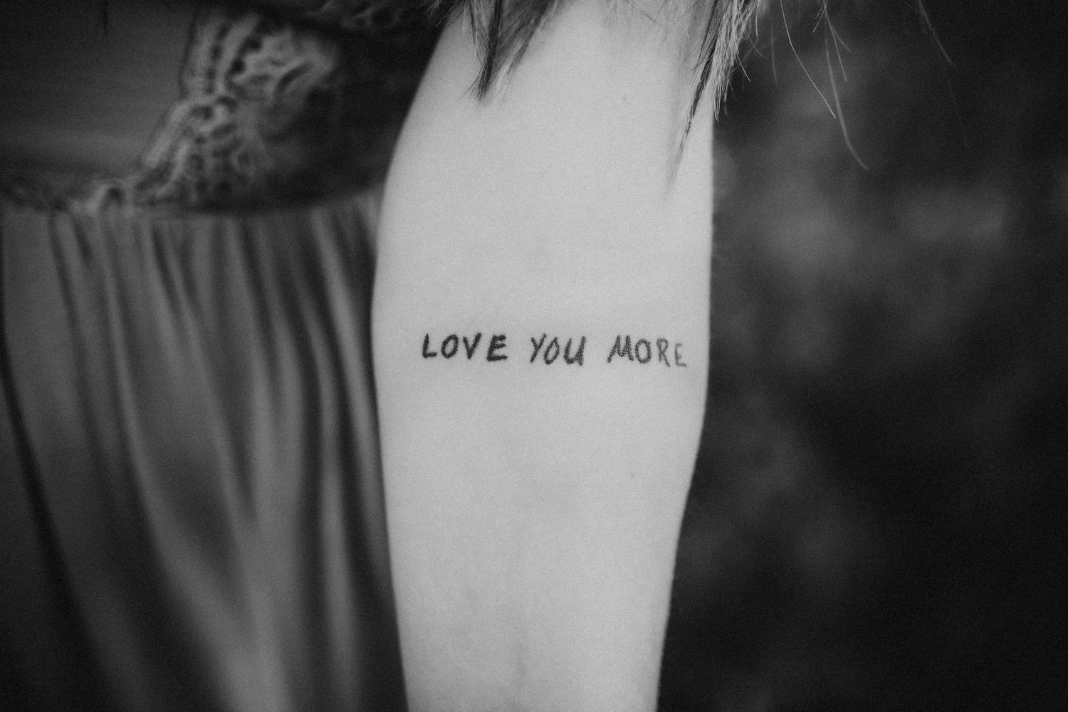 A woman holds out her arm and shows a tattoo that says Love You More.