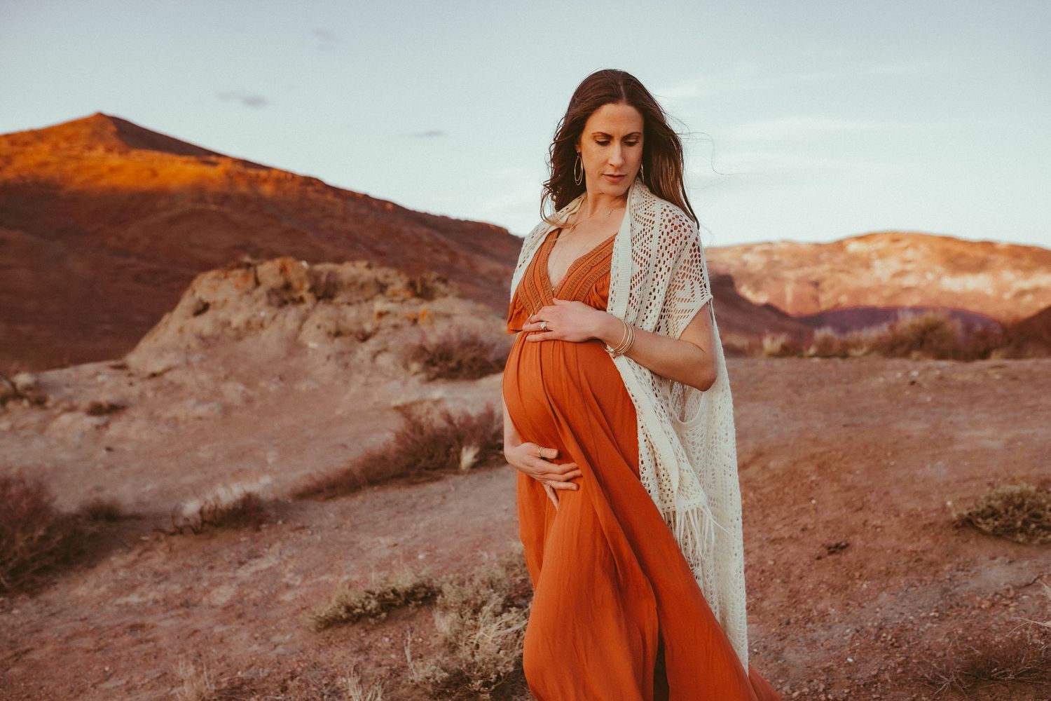 A pregnant mother in a red dress stands cradling her growing belly, photographed by Kristy Baker Photography in Steamboat Springs, Colorado.