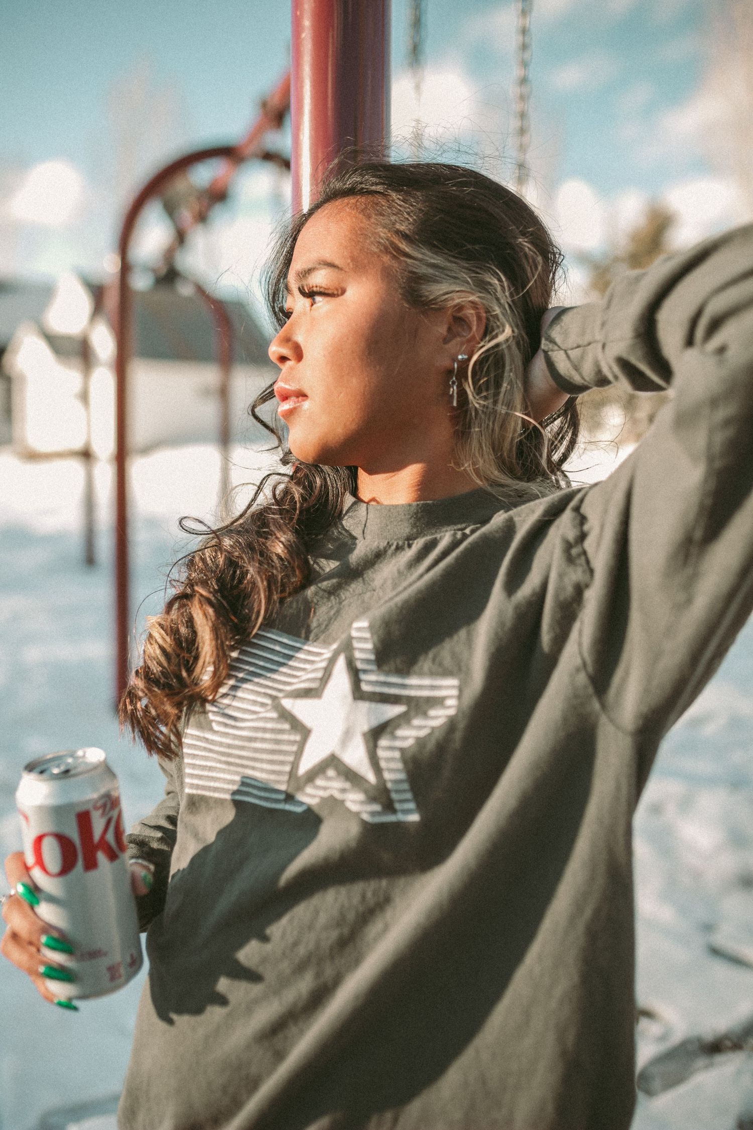 A woman drinking a Diet Coke is at the park and looking towards the sun.