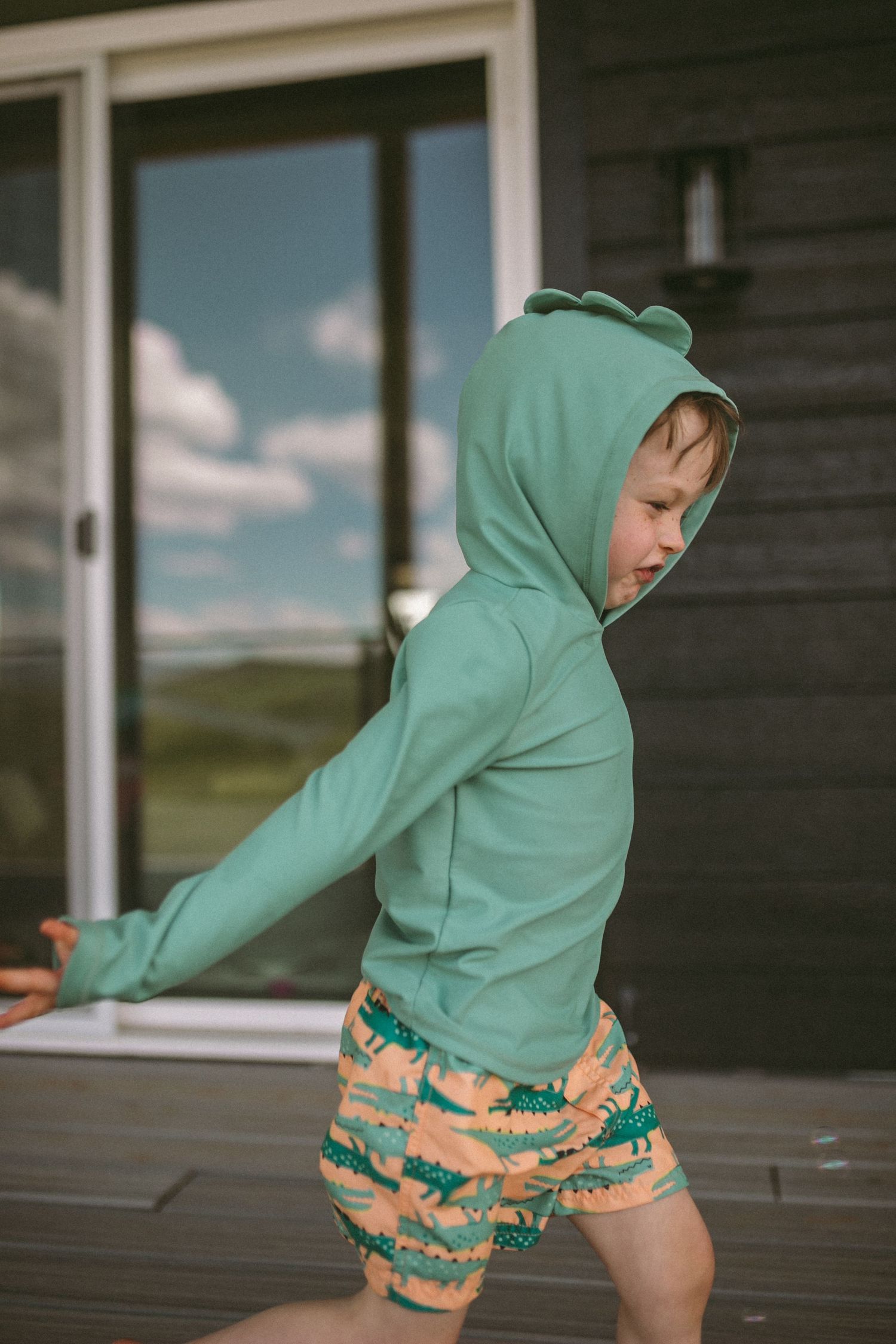 A young boy in his swim suit is running passed a sliding glass door, photographed by Kristy Baker Photography.