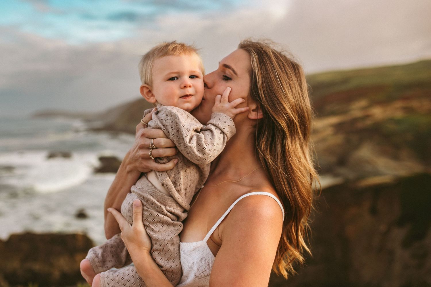 A mother holds her young son and kisses him on the cheek, photographed by Kristy Baker Photography.