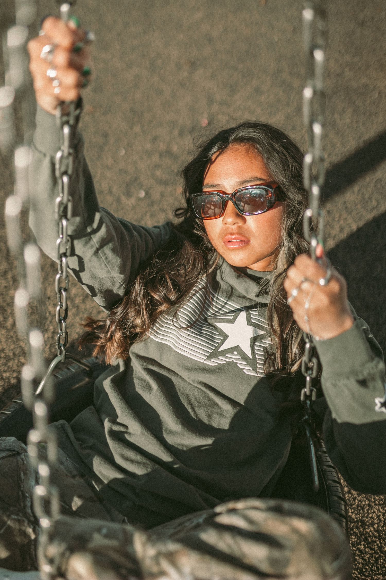 A woman wearing sunglasses sits in a tire swing and looks at the camera lens.