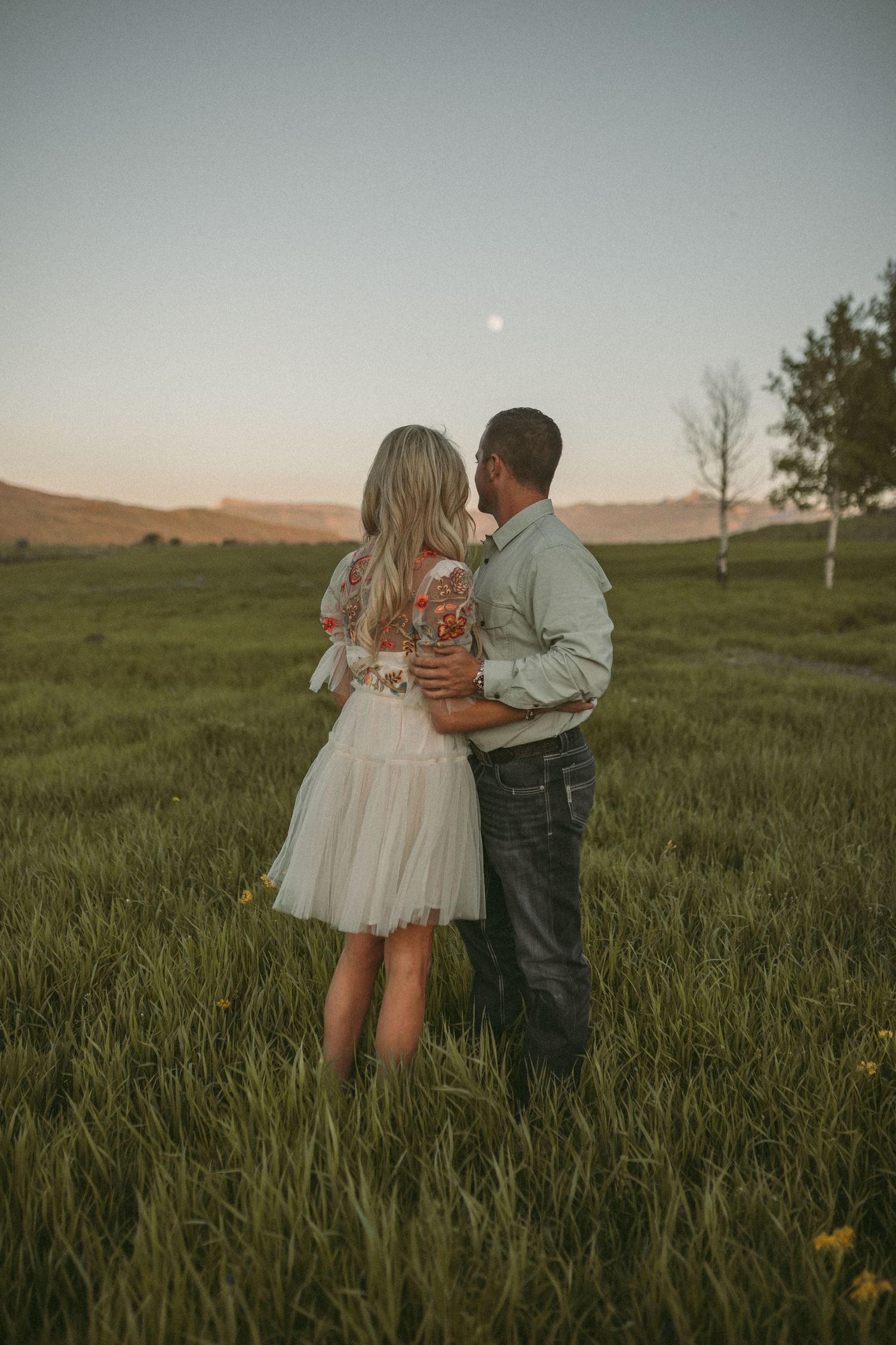 A couple standing together looking out at the moon at dusk, photographed by Kristy Baker Photography in Steamboat Springs, Colorado.