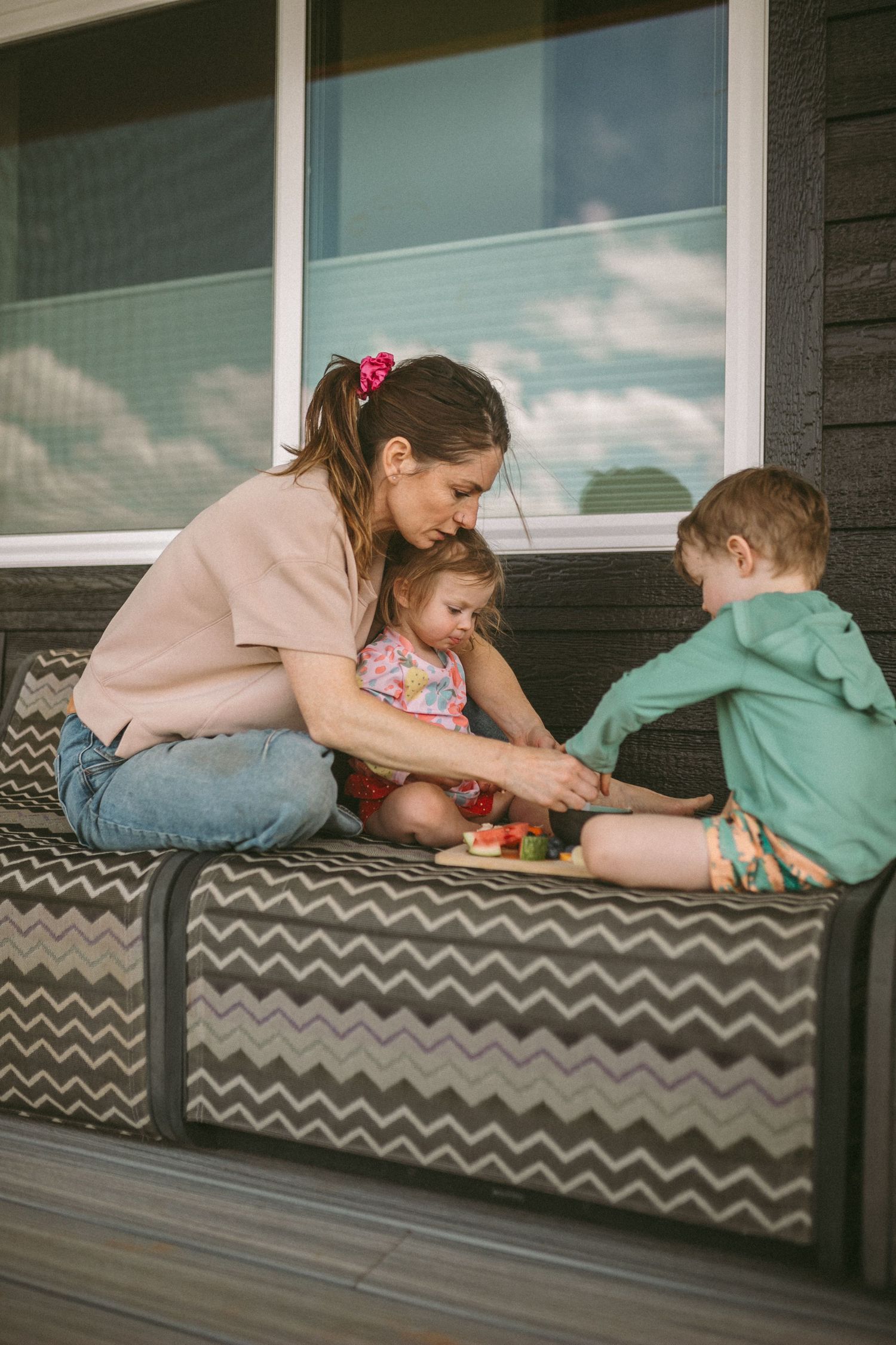 A mother sits with her two children on the deck chairs, photographed by Kristy Baker Photography.