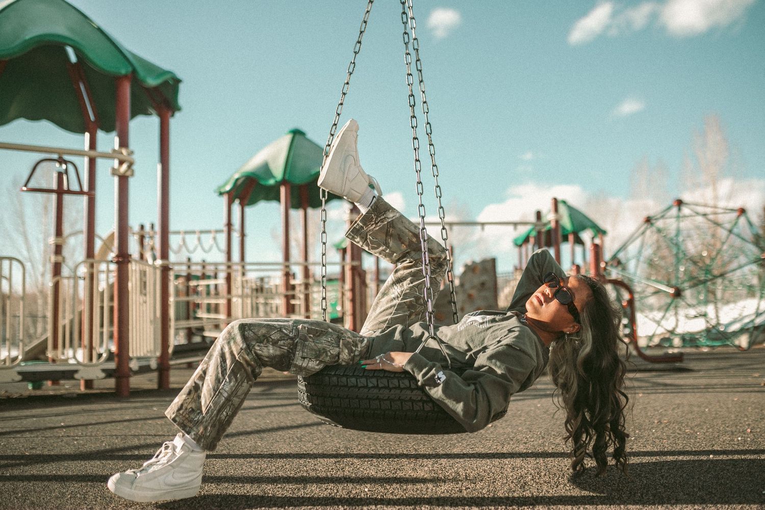 A woman is laying down swinging in a tire swing at a park.