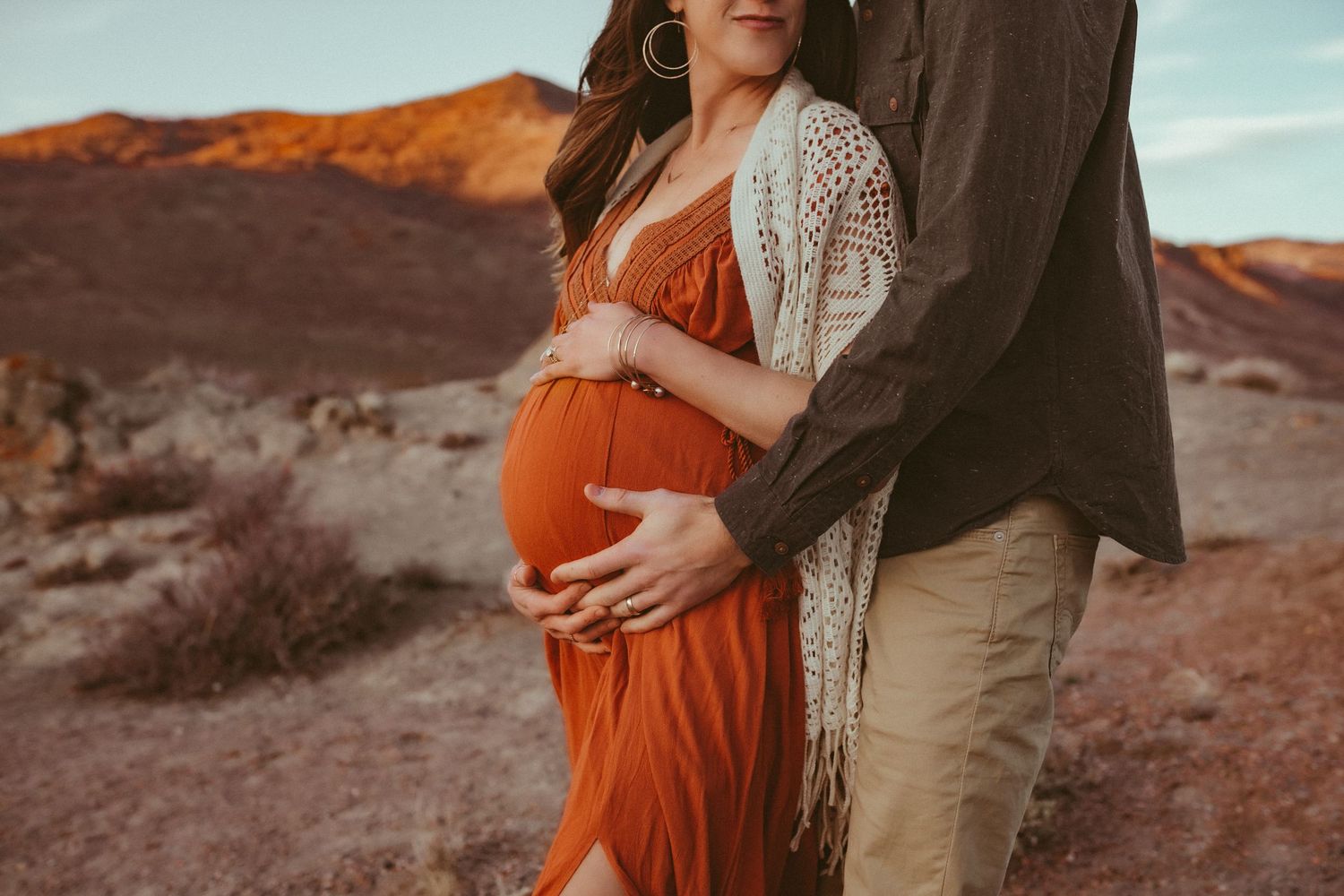 A pregnant mother is standing with her husband as they cradle her belly, photographed by Kristy Baker Photography in Steamboat Springs, CO.
