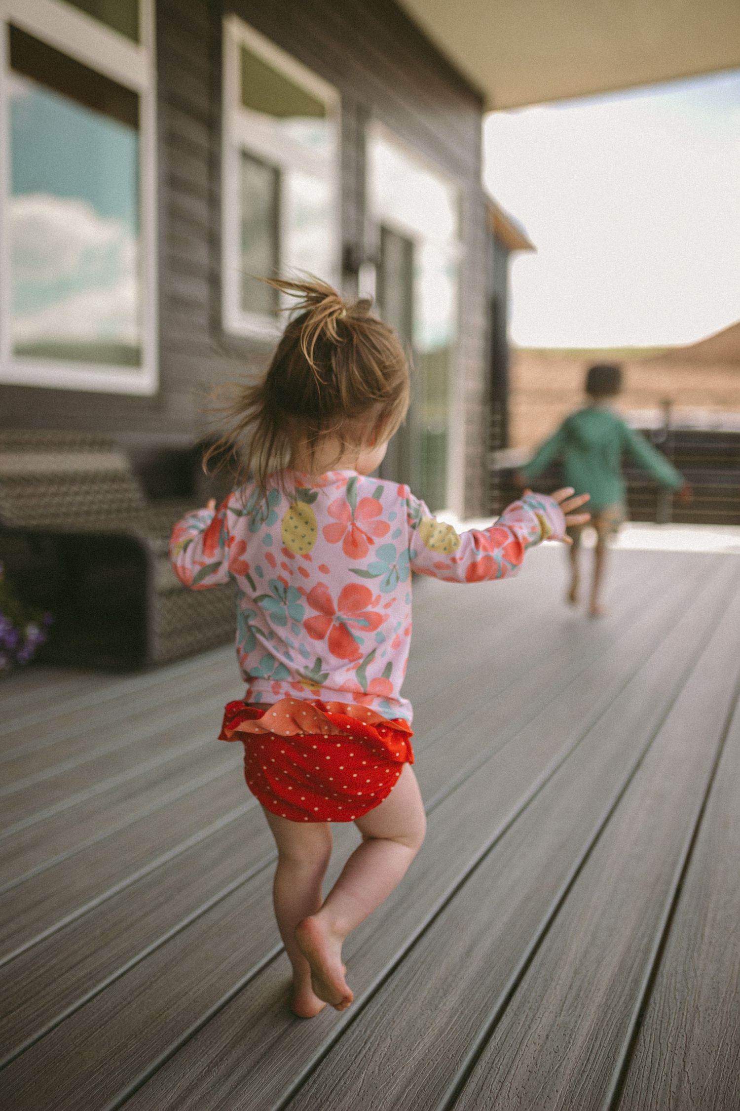 A small girl is running away from the camera following behind her older brother, photographed by Kristy Baker Photography.