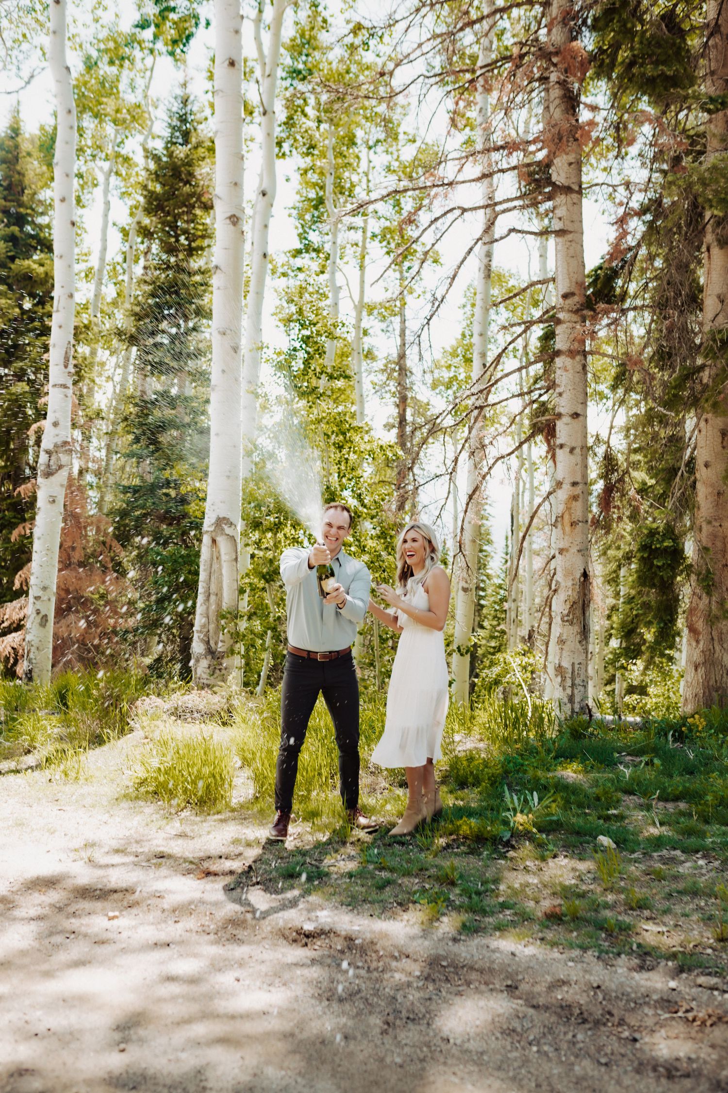 A couple celebrating their engagement by spraying champagne, photographed by Kristy Baker Photography in Steamboat Springs, Colorado.