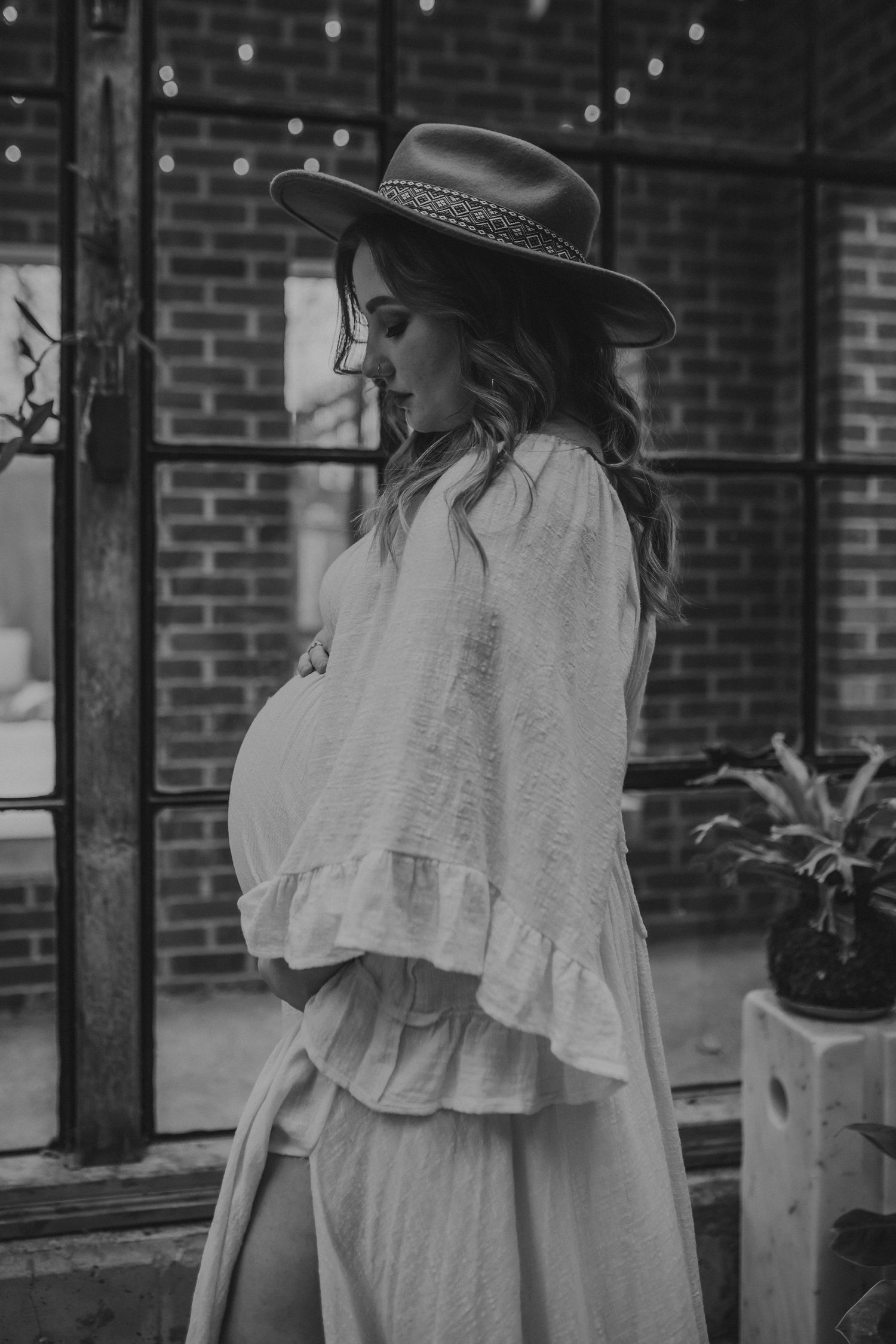 A pregnant mother stands inside a brick building looking down at her belly, photographed by Kristy Baker Photography.
