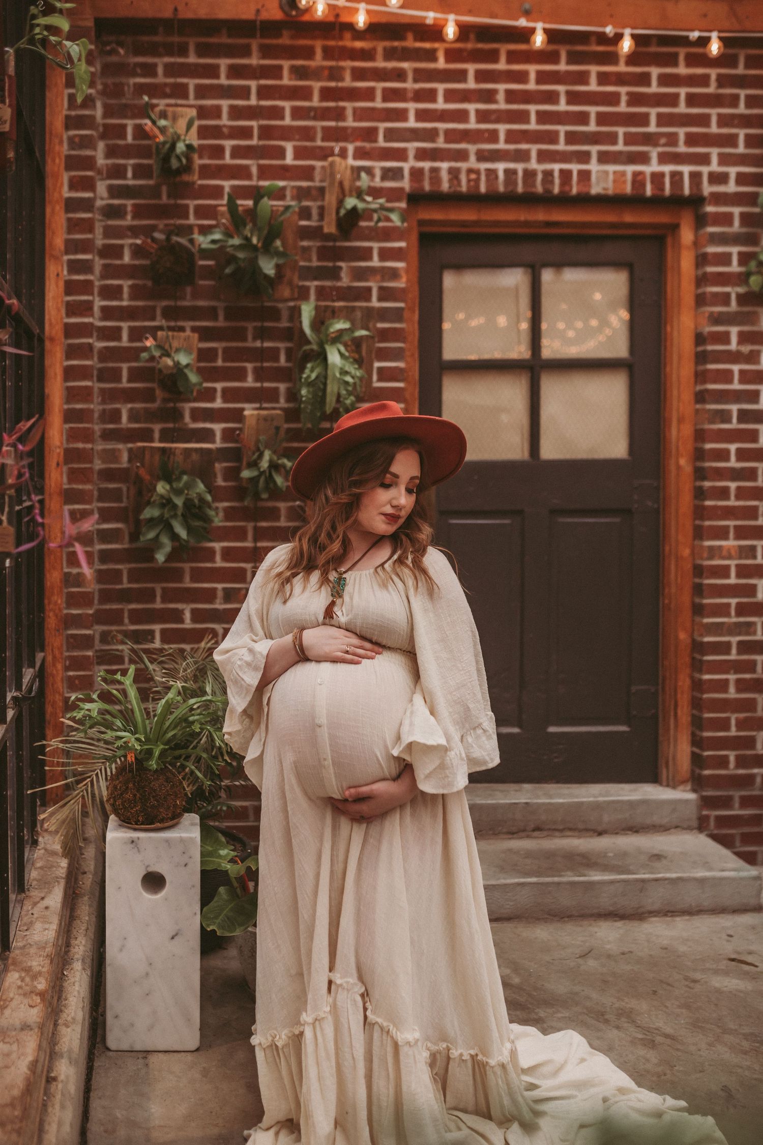 A pregnant mother stands inside a brick building looking down at her belly, photographed by Kristy Baker Photography.