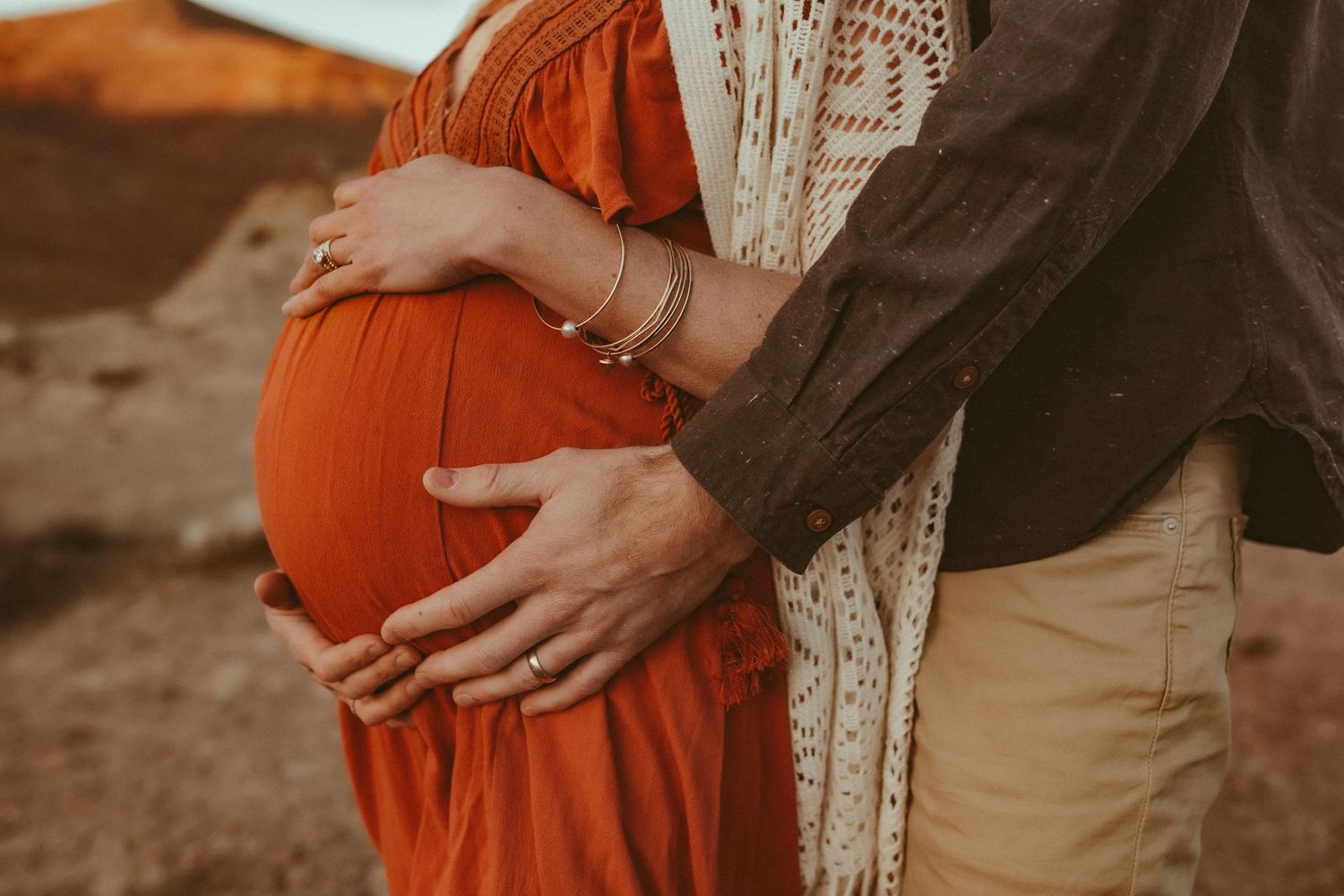 A pregnant mother cradling her belly with her husband standing behind her, photographed by Kristy Baker Photography.
