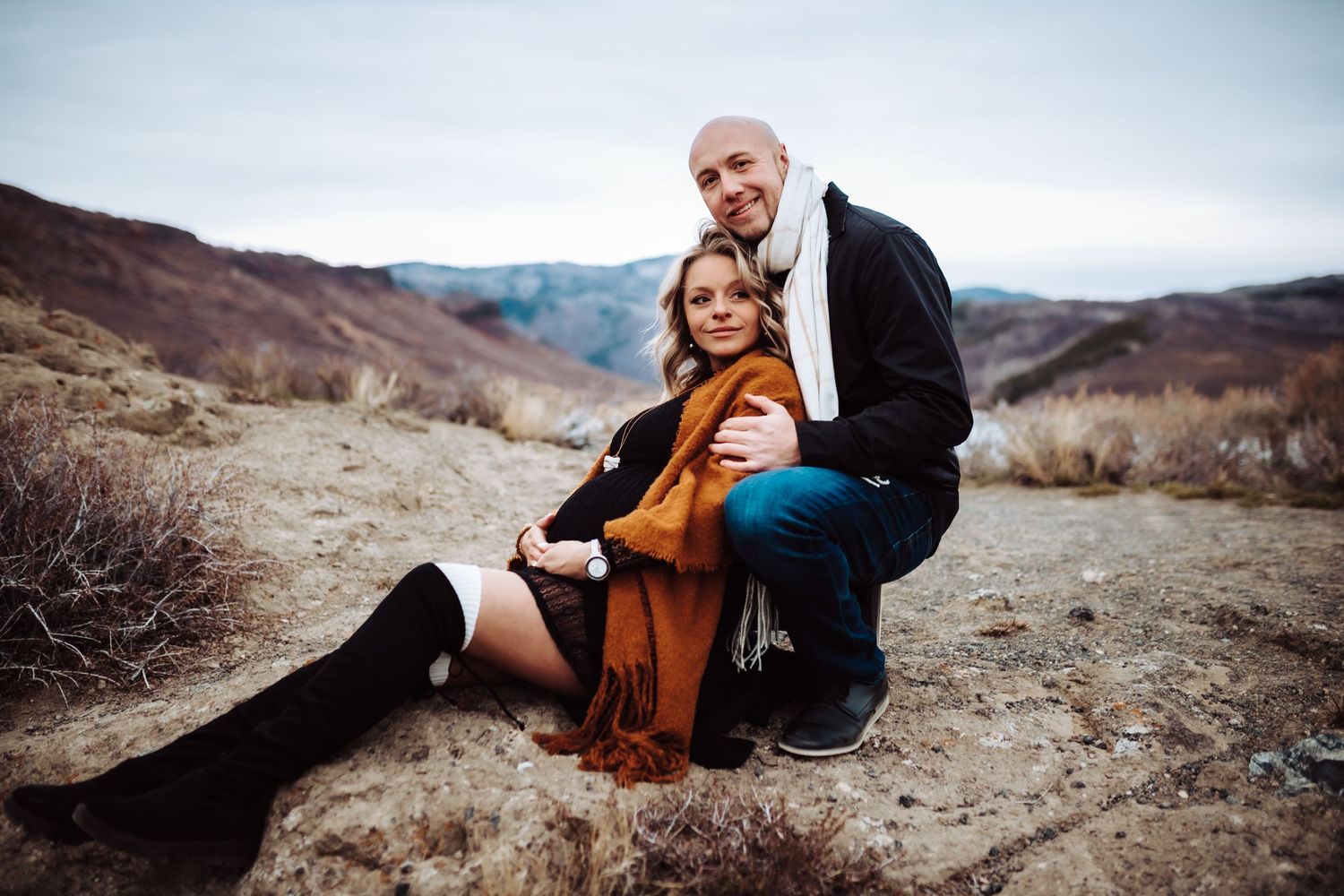 A pregnant woman sits and cradles her belly as her husband kneels behind her, photographed by Kristy Baker Photography in Steamboat Springs.