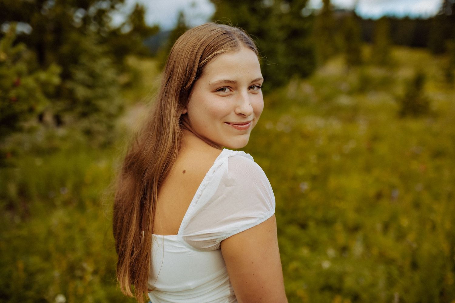 A high school senior girl wearing a white shirt is smiling a looking over her shoulder.