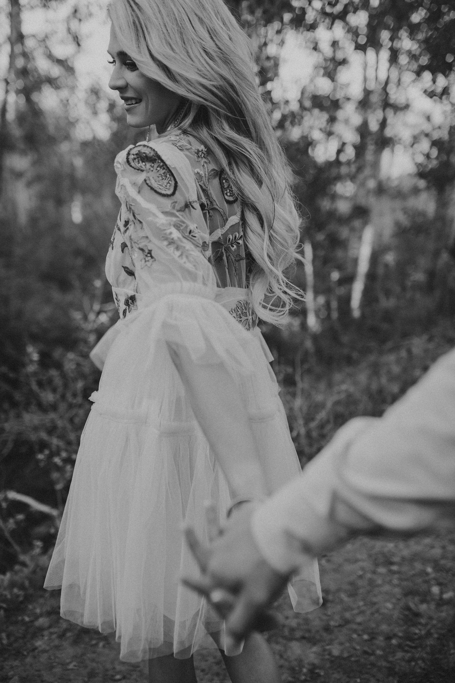 A woman is walking and looking back while holding hands, photographed by Kristy Baker Photography in Steamboat Springs, Colorado.