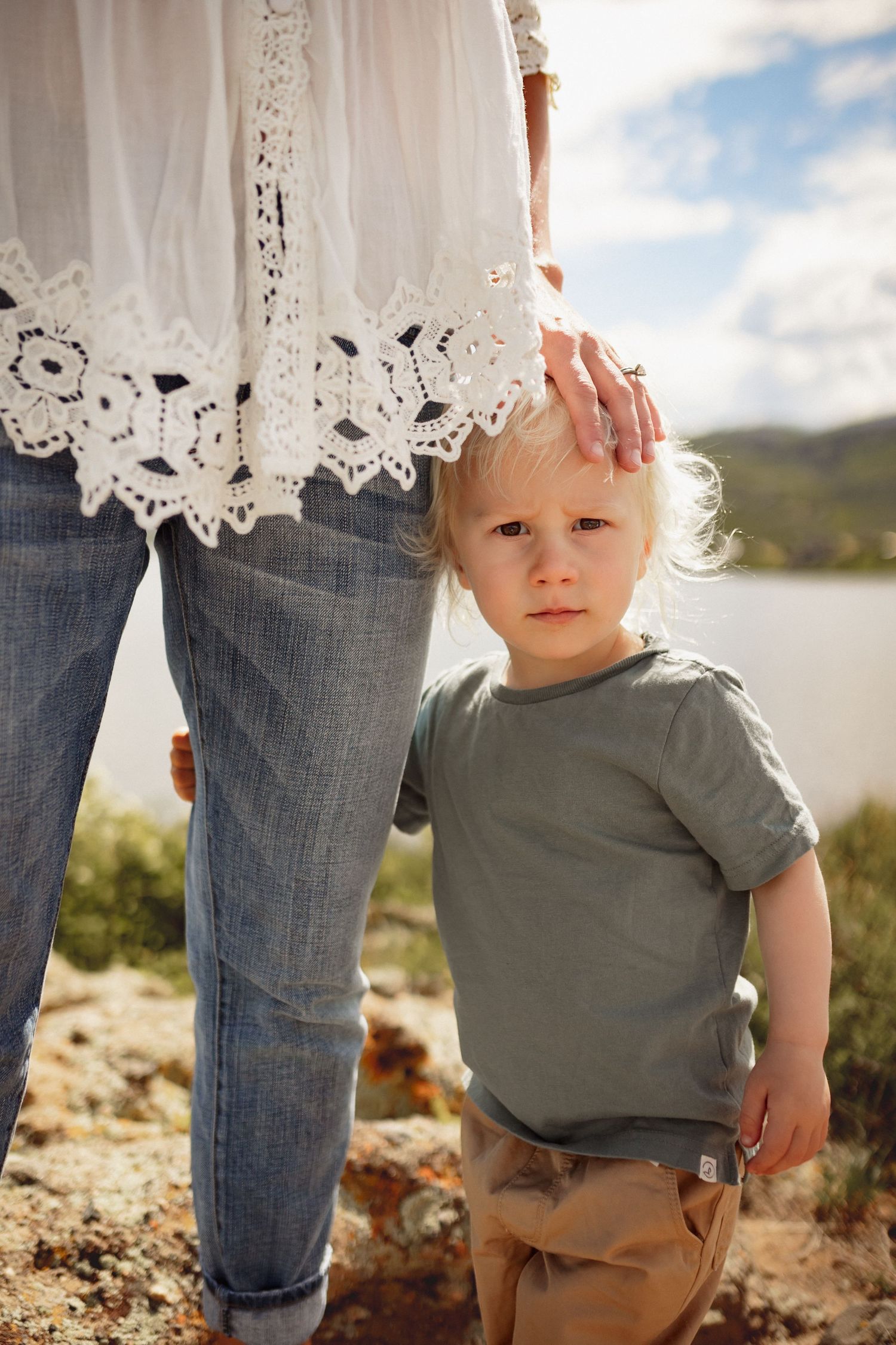 A young boy holds onto his mother's leg and looks right into the camera, photographed by Kristy Baker Photography.
