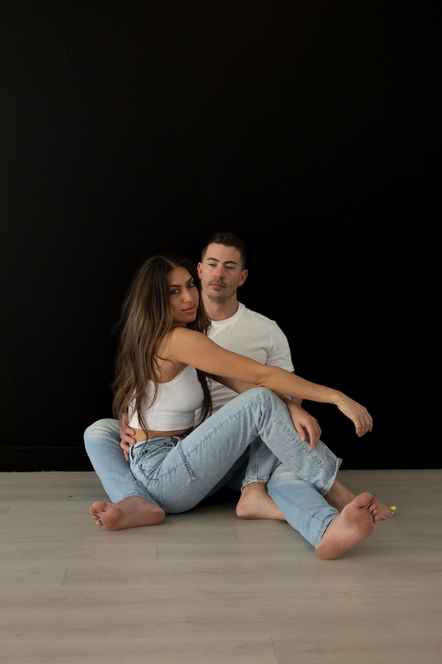 Editorial-style Oklahoma engagement portrait of a couple wearing classic white shirts and jeans in a studio setting with a black backdrop. A