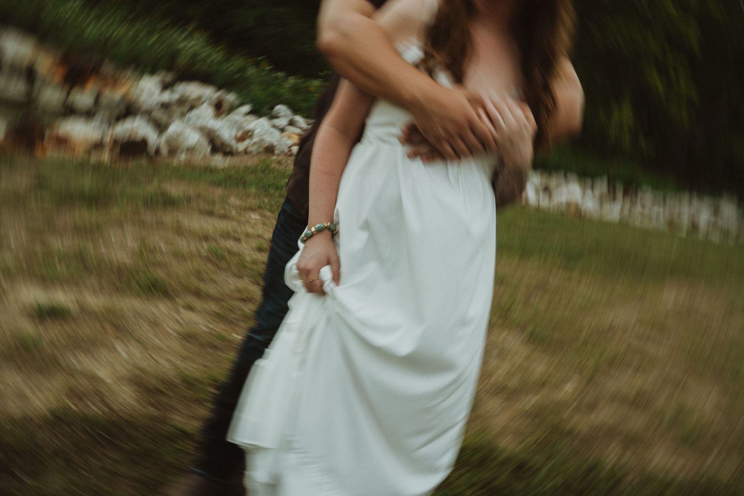 Couple embracing outdoors in a romantic blurred motion shot, woman in white wedding dress on grassy field.
