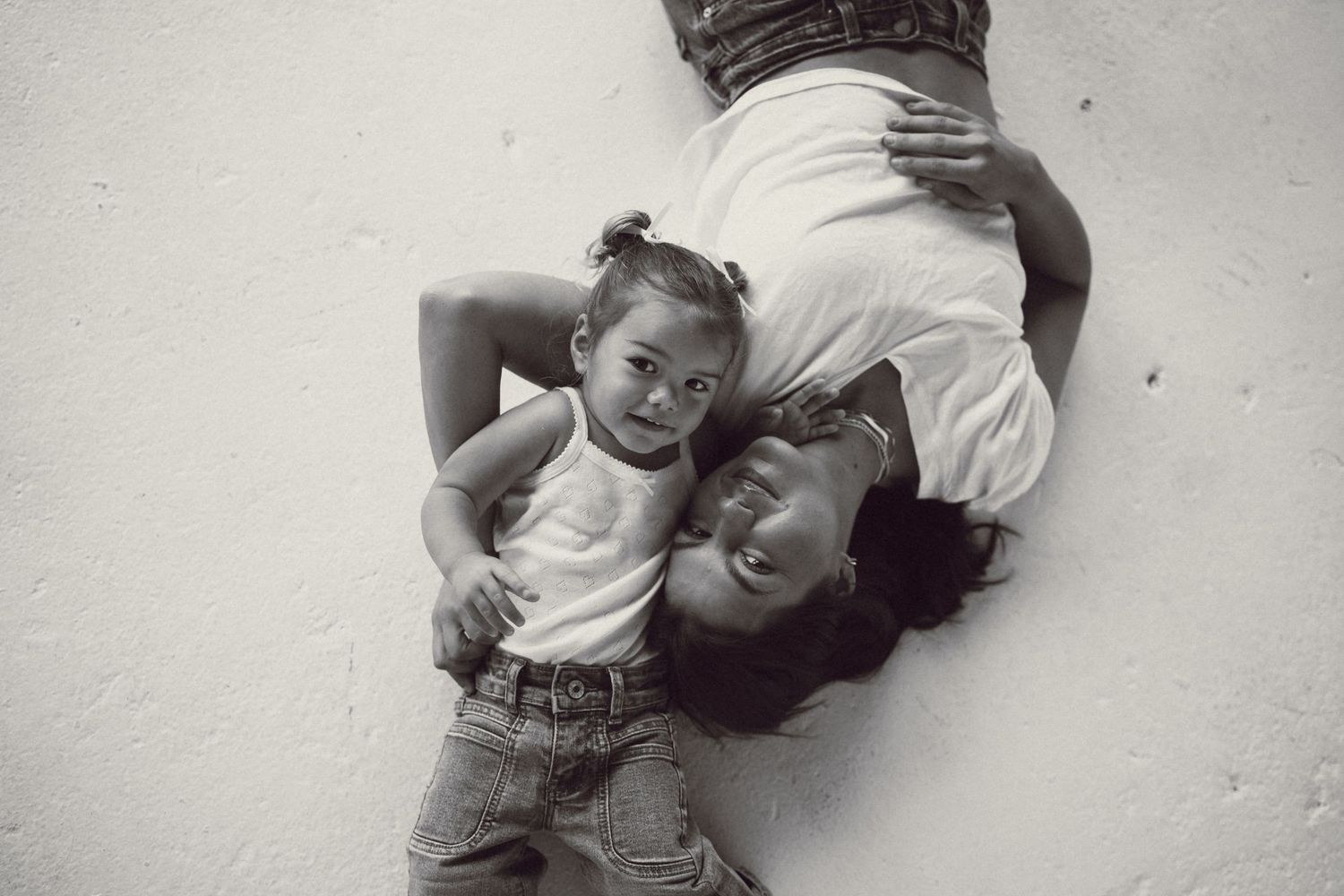 Black and white photo of a mother and young child lying on the floor, smiling and embracing in a tender moment.