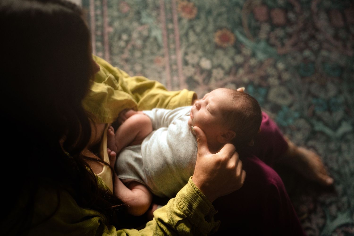 A mother cradles her sleeping newborn baby in her arms in a warmly lit room.
