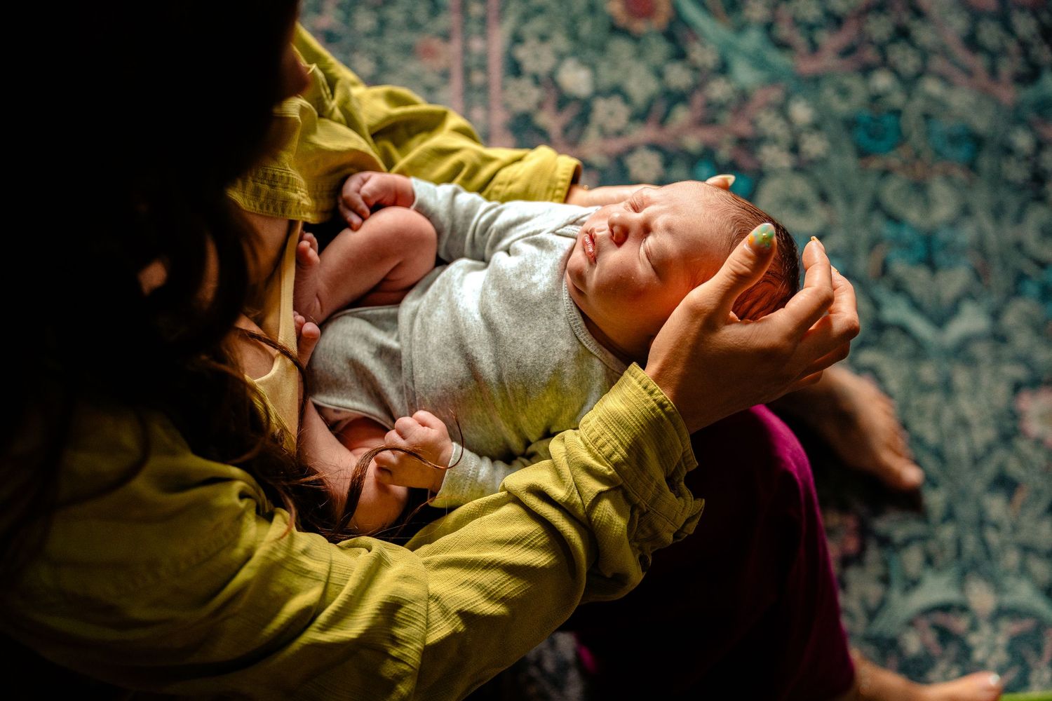 A mother tenderly cradles her newborn baby in her arms against a floral background.