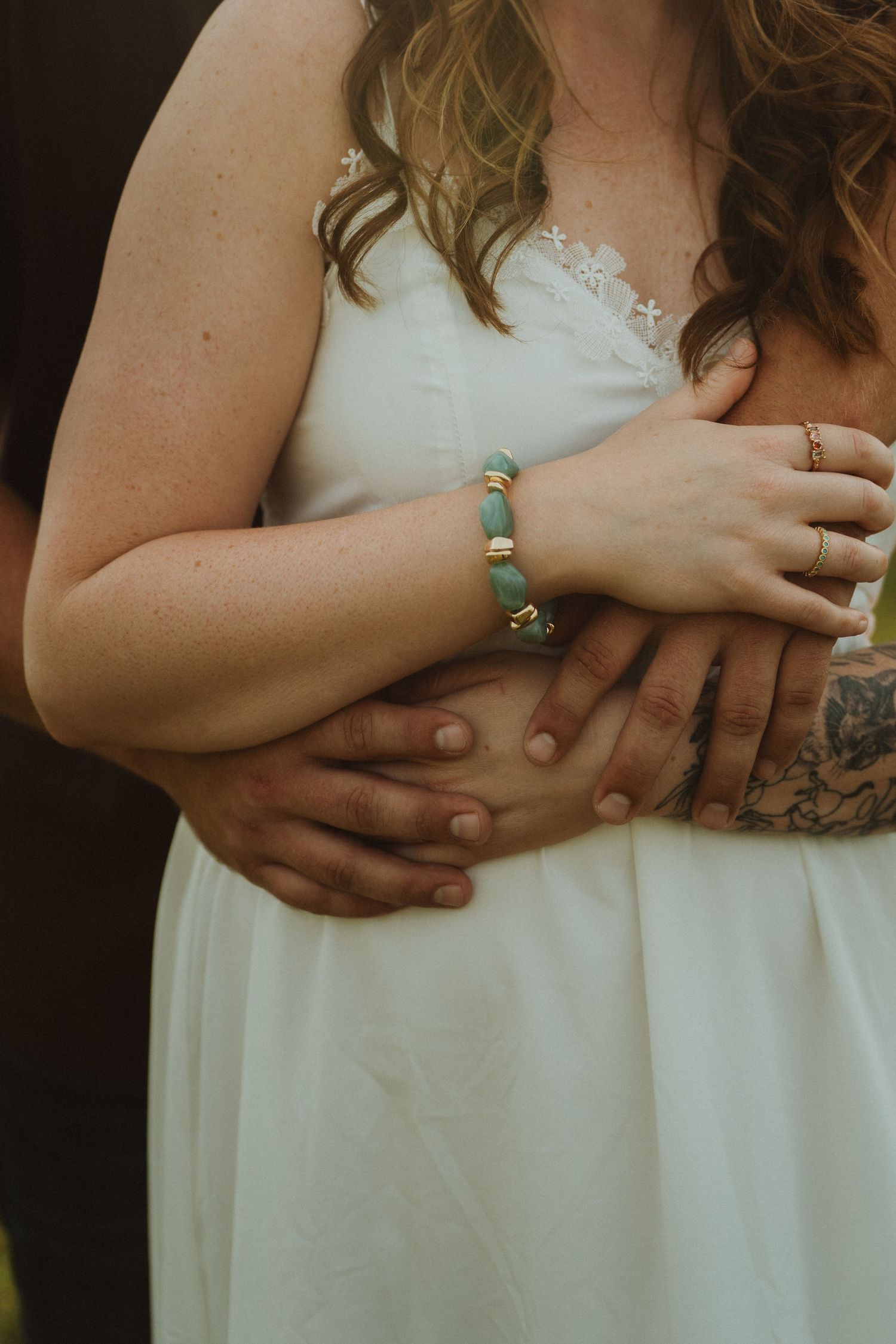 Bride in white dress with turquoise bracelet and ring, hands clasped with tattooed partner at wedding.
