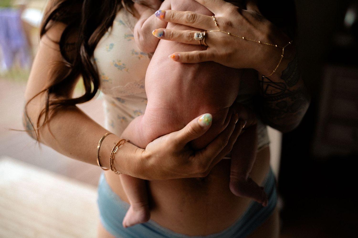Close-up of mother with gold bracelets and rings gently cradling naked newborn baby.