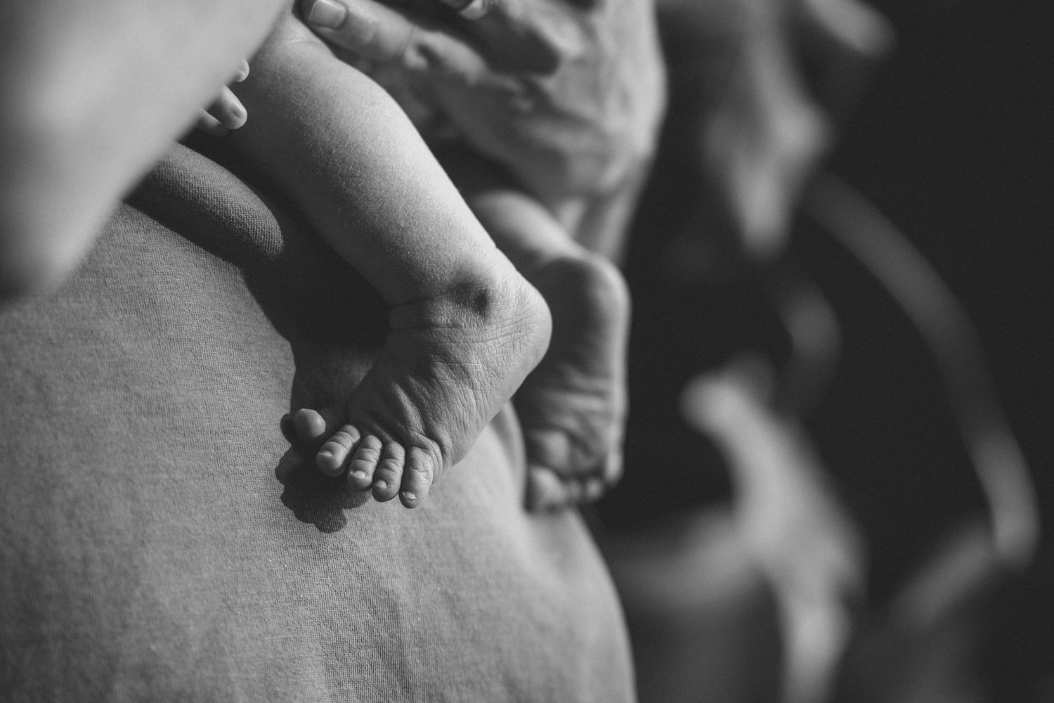 Black and white close-up of tiny newborn baby feet resting on parent lap.