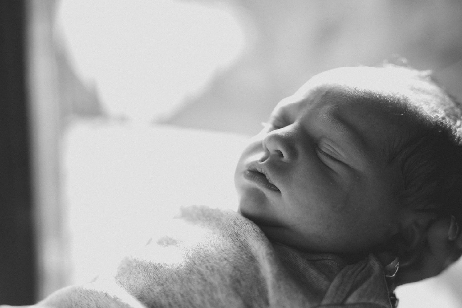 Black and white newborn baby sleeping peacefully, wrapped in soft blanket, serene infant portrait photography.