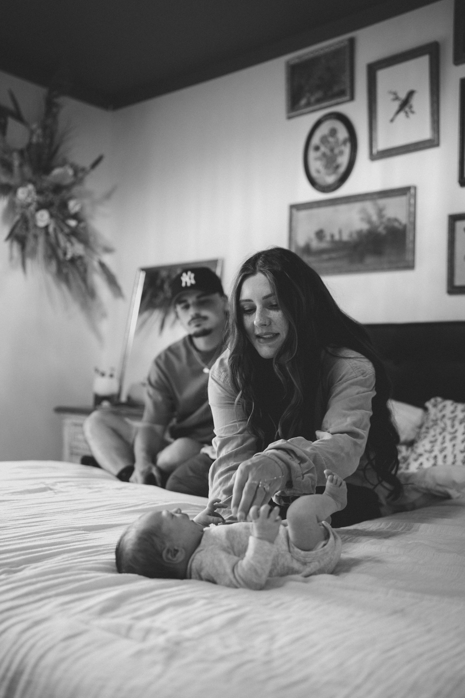 Black and white photo of parents with their newborn baby on a bed in a cozy decorated bedroom.