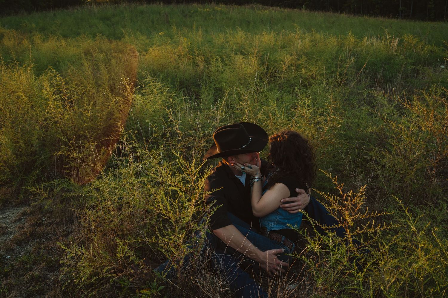 Couple sharing a romantic moment sitting together in a lush green field at golden hour.
