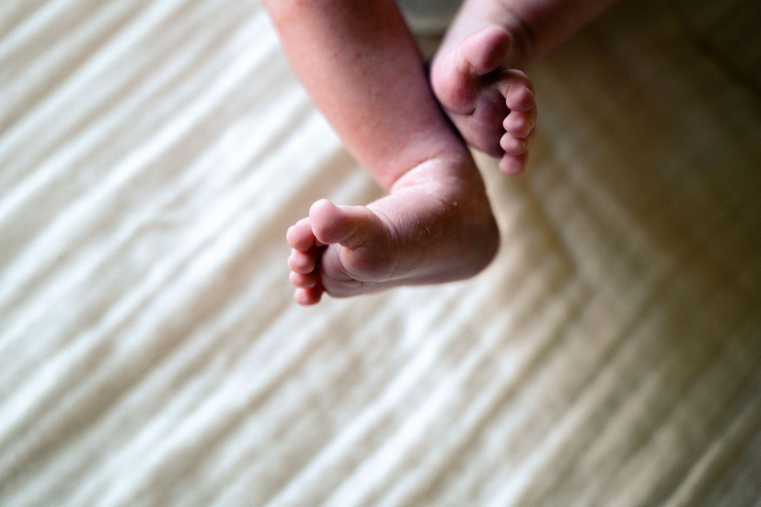 Close-up of delicate newborn baby feet resting on a cream textured blanket.