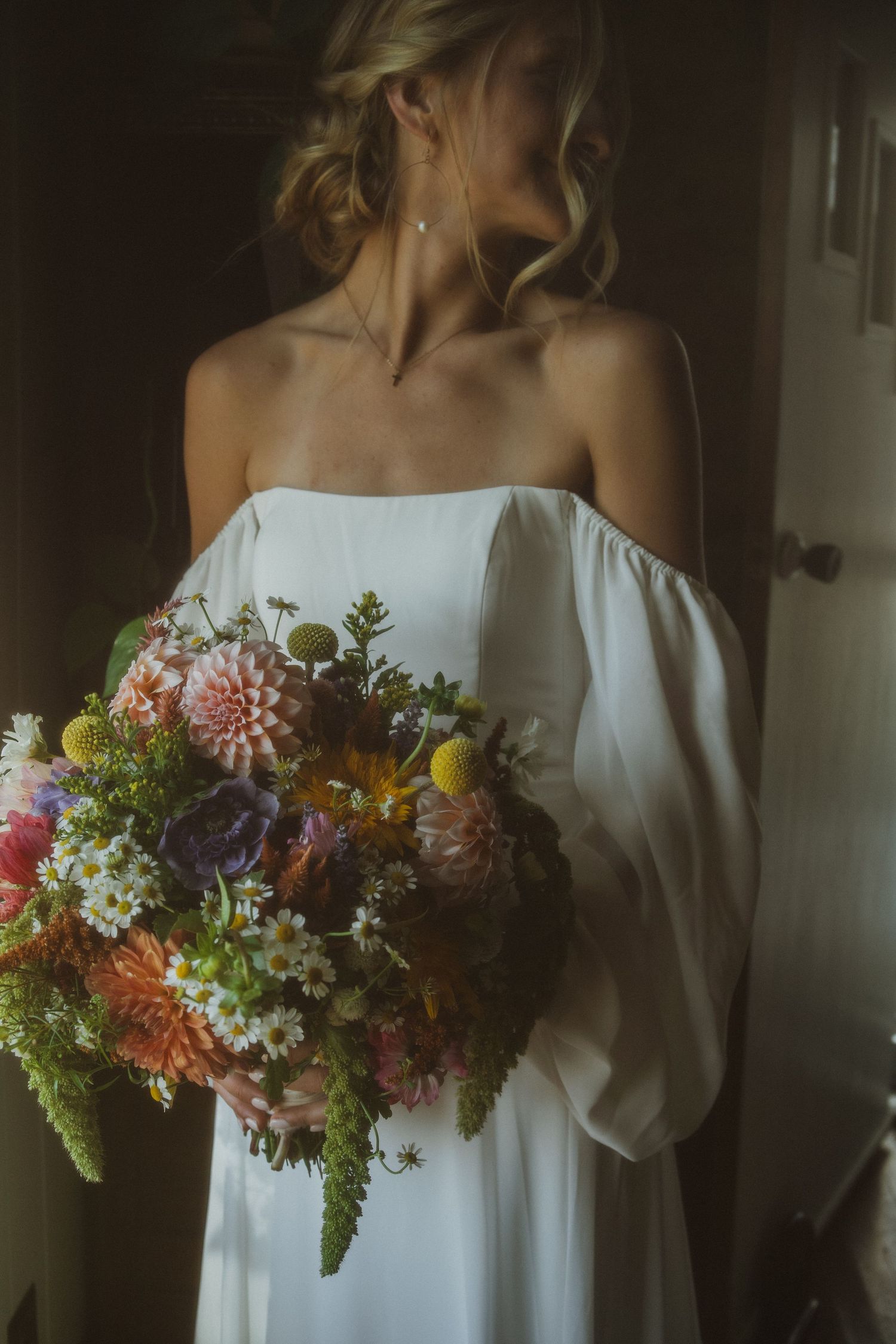 White off-shoulder dress adorned with vibrant wildflower bouquet in moody lighting.